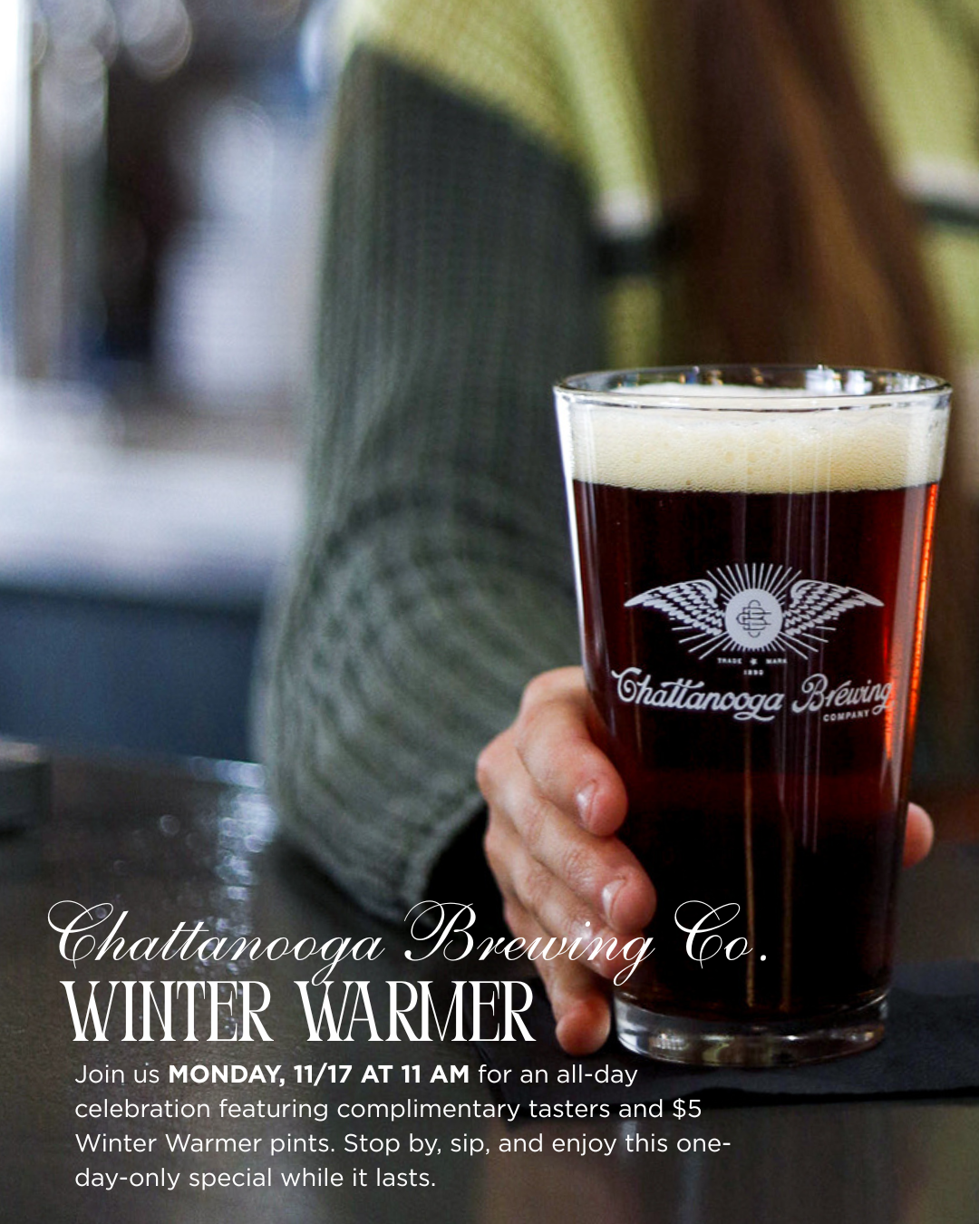 A pint of dark beer with a cream-colored head held by a person wearing a green sweater. The glass has a Chattanooga Brewing Company logo. Text on the image promotes a Winter Warmer event at Chattanooga Brewing Co., with complimentary tasters, $5 Wint