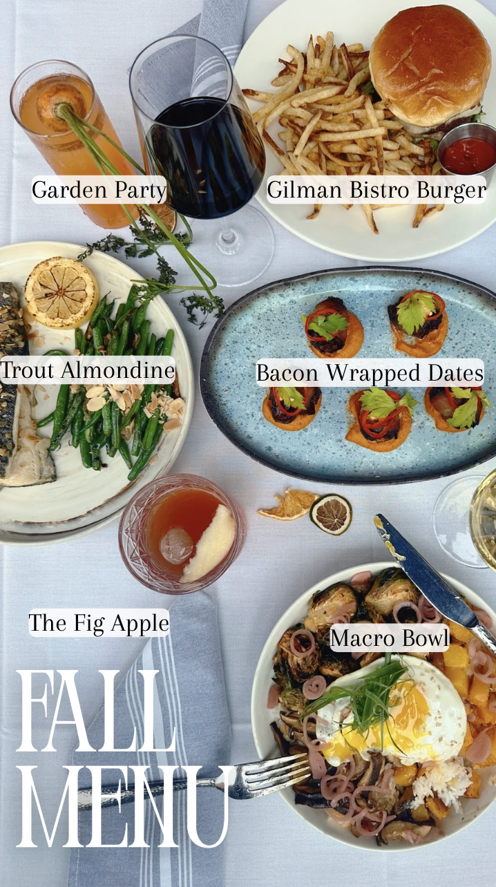 A table set with various fall-themed dishes and drinks, including a grilled bistro burger with fries, a bowl of trout almondine, bacon-wrapped dates, a macro bowl with an egg, and a slice of fig apple. Beverages include wine, a cocktail, and a soft d