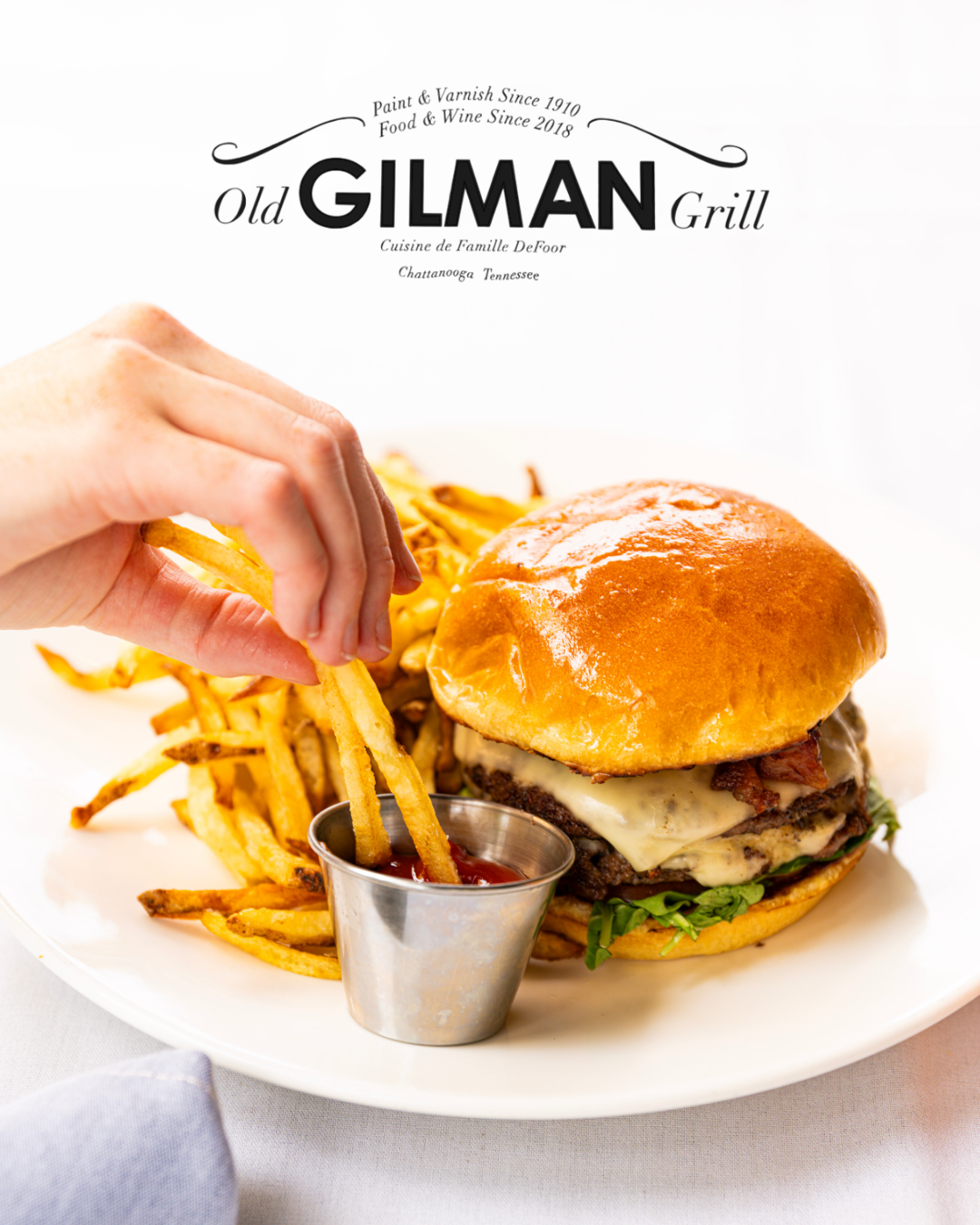 A cheeseburger with lettuce, cheese, and bacon on a brioche bun with a side of French fries and ketchup.