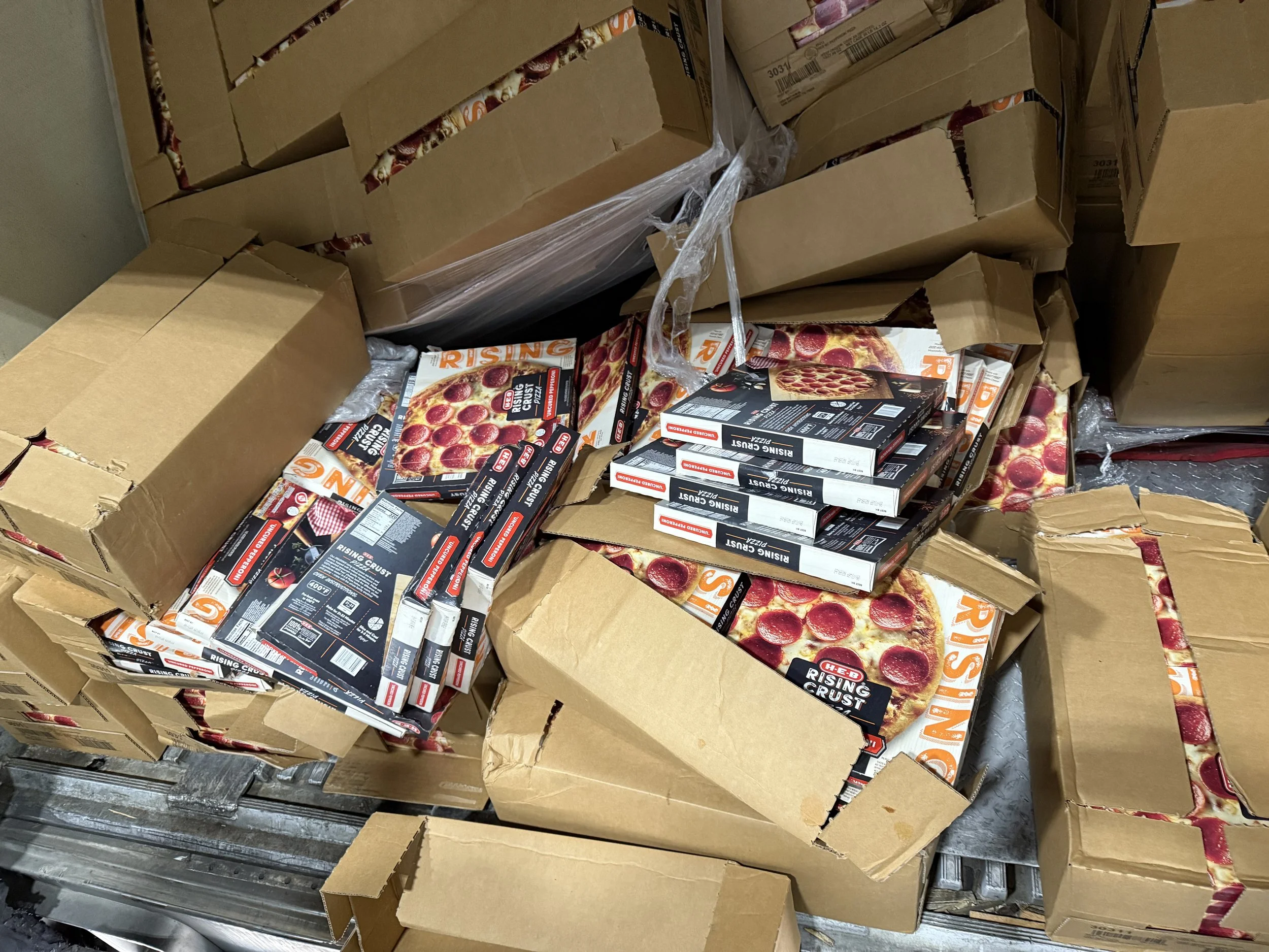 Cardboard boxes and pizza boxes piled together, with some boxes open showing frozen Rising crust pizza packaging inside.