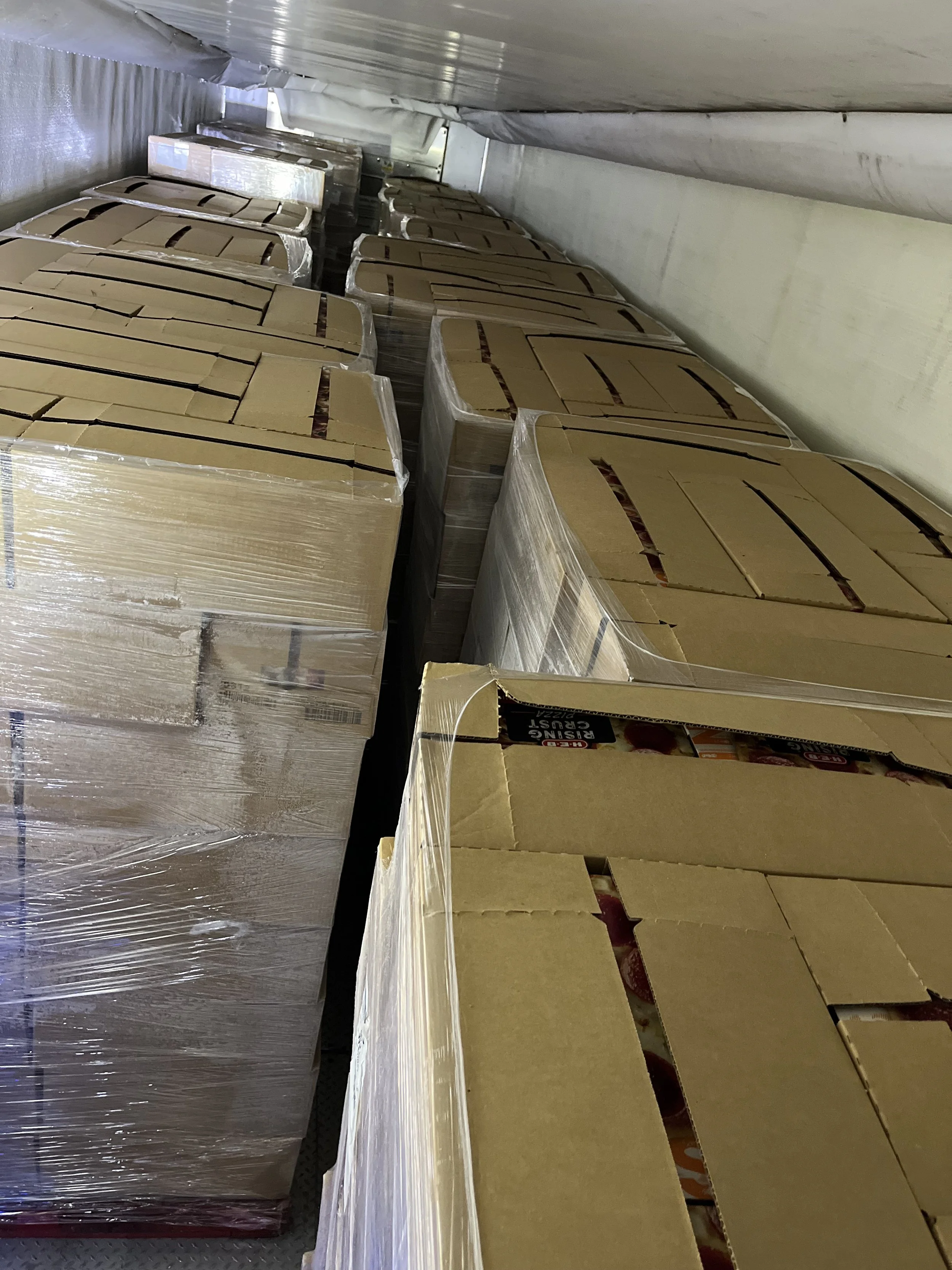 Stacks of cardboard boxes wrapped in plastic in a narrow industrial storage area.