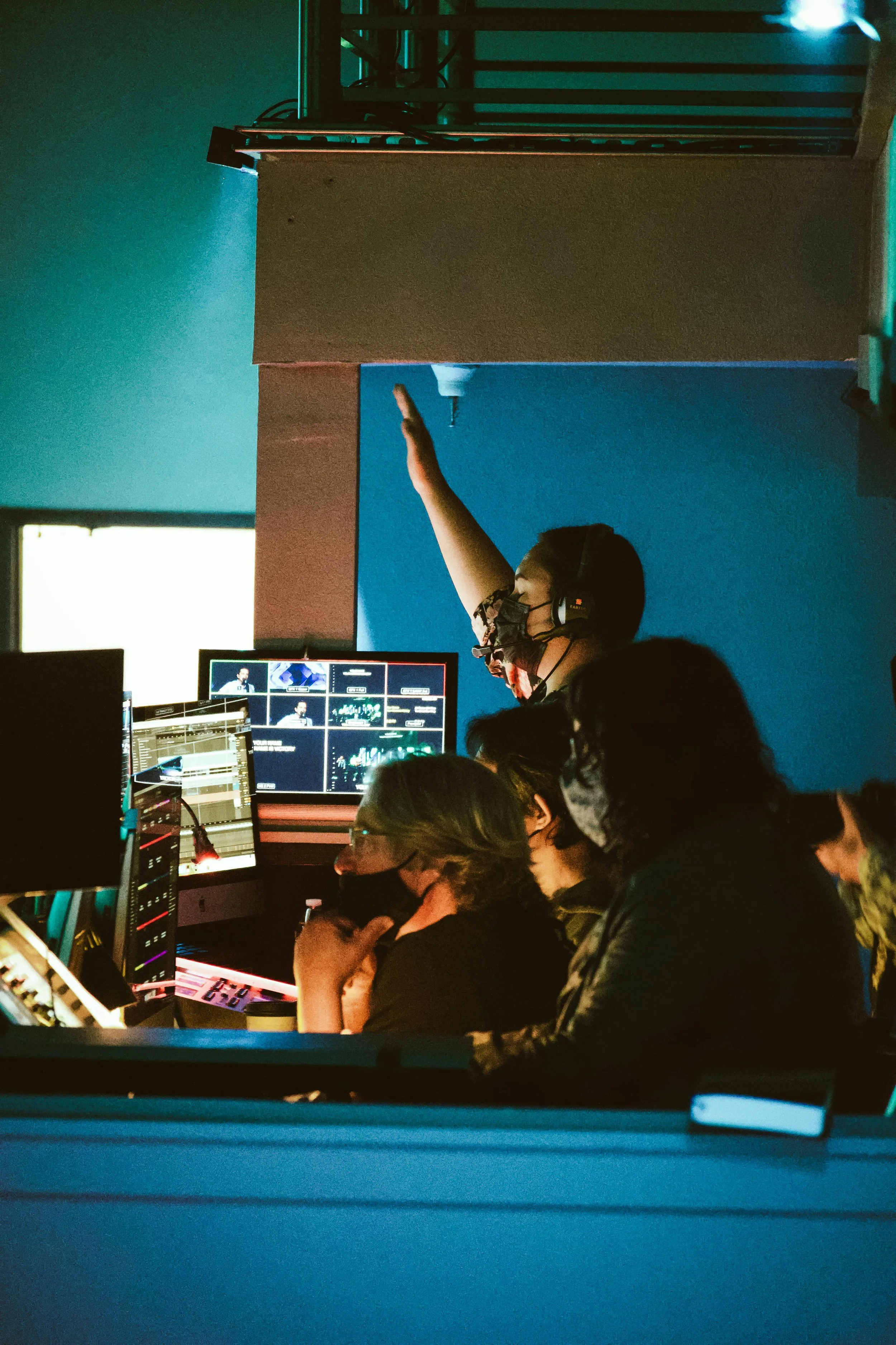 People in a control room with computers and monitors, working together in a darkened environment.