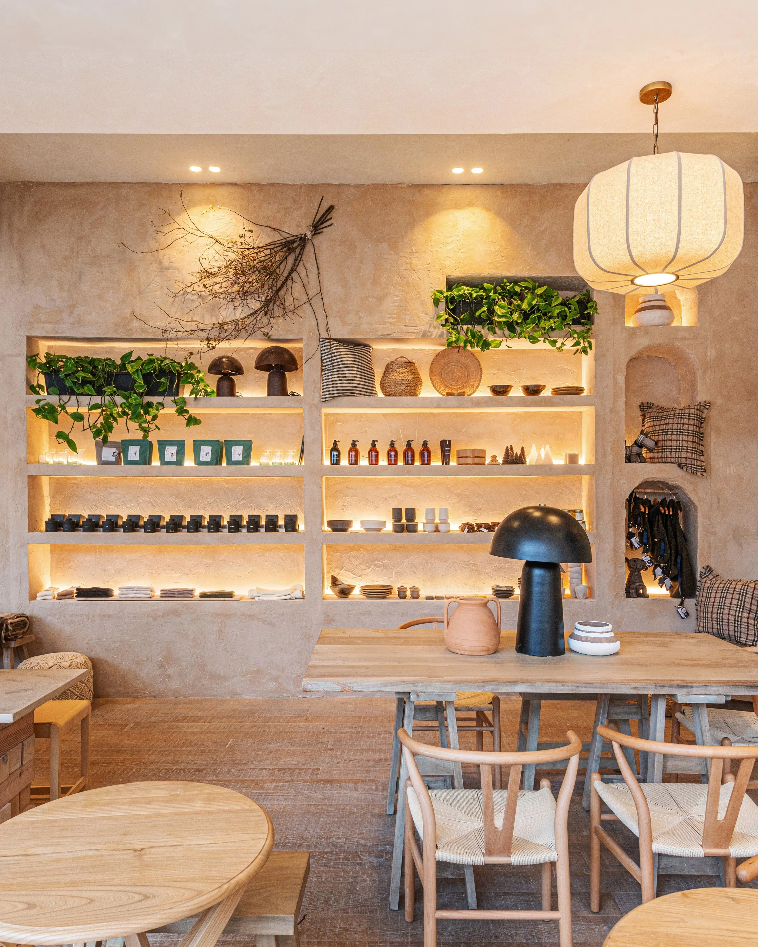 Interior of a cozy, modern room with built-in shelves displaying decorative items, plants, and ceramics, with a wooden table and chairs, warm lighting, and a hanging paper lantern by WOLFOX and LOAFT
