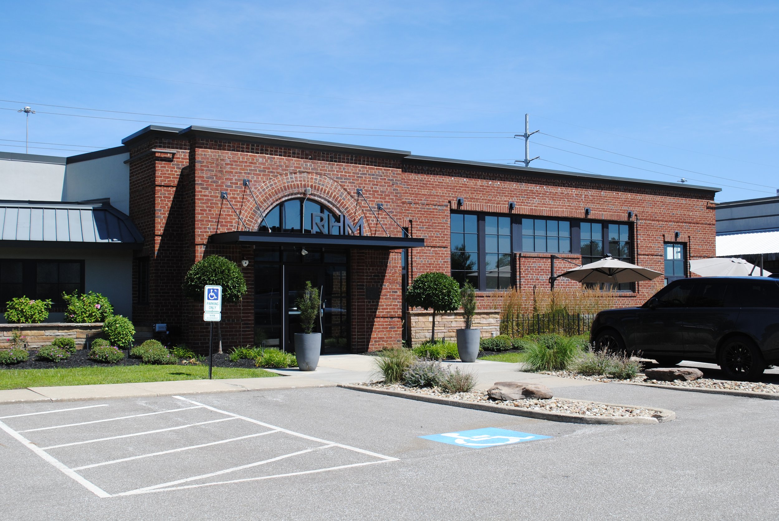 Brick commercial building with large windows, landscaping, and a parking lot including designated accessible parking space and handicap sign.