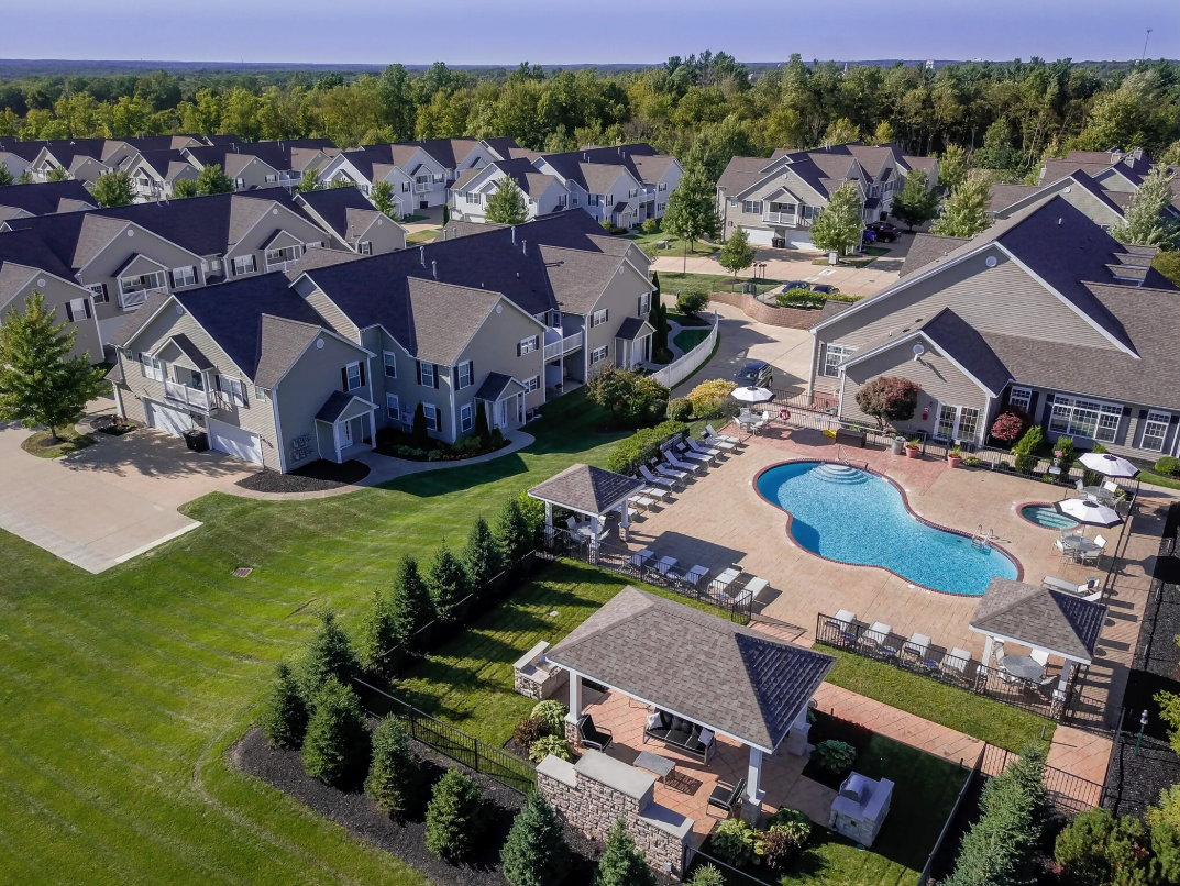 Aerial view of a community with multiple residential houses, a swimming pool, and landscaped green areas.