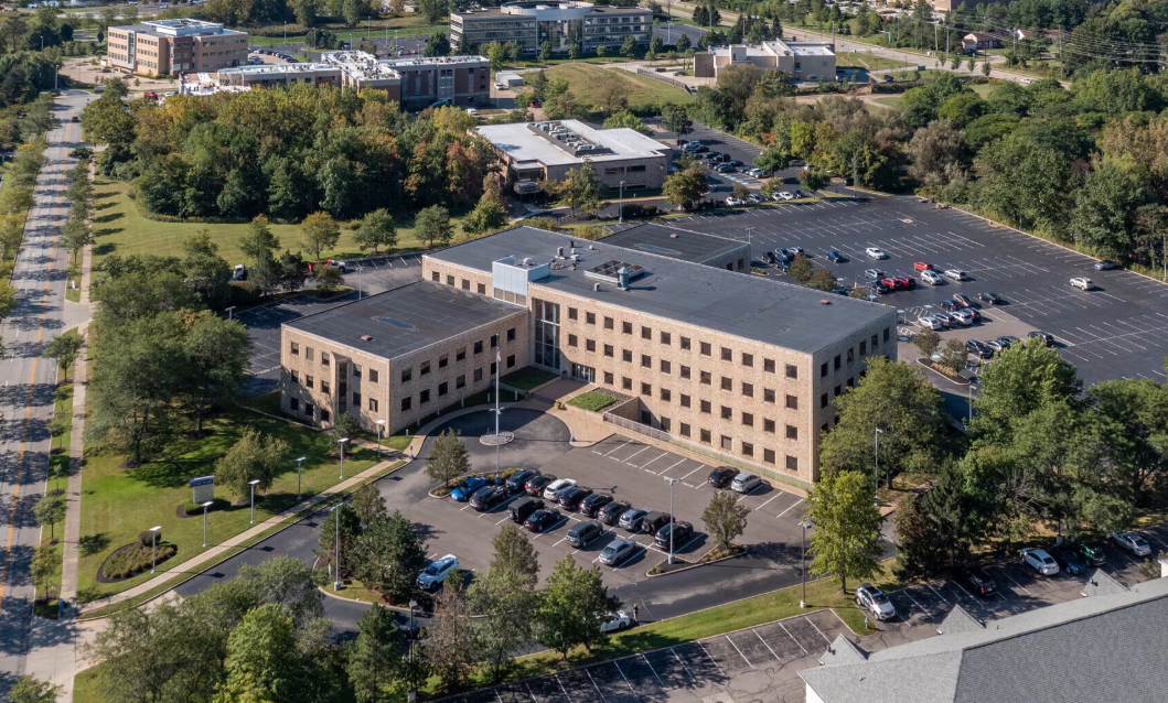 Aerial view of a large office building with parking lots surrounded by trees and other buildings.
