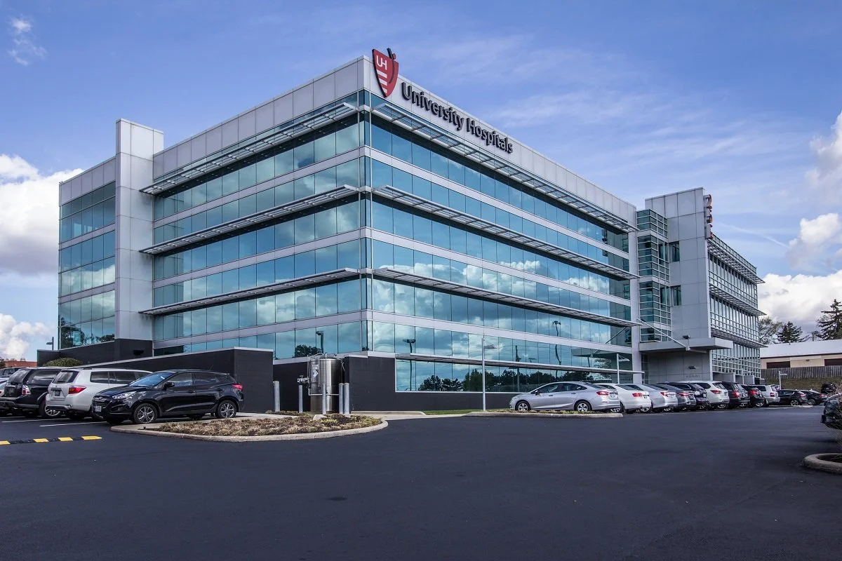 Modern multi-story hospital building with glass windows and parking lot in front