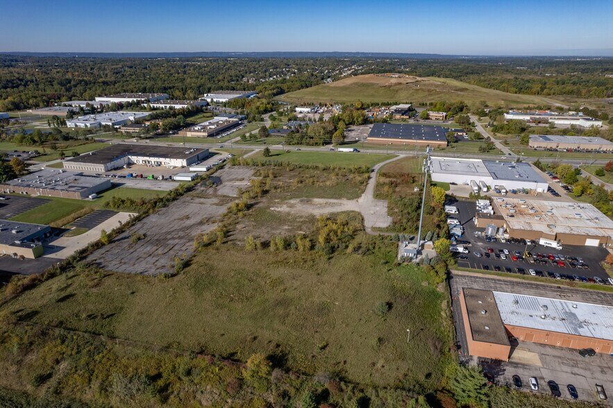 Aerial view of a commercial and industrial area with vacant lots, roads, and parking lots, surrounded by greenery and hills in the background.
