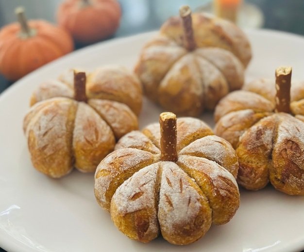 Pumpkin-shaped bread rolls dusted with powdered sugar on a white plate
