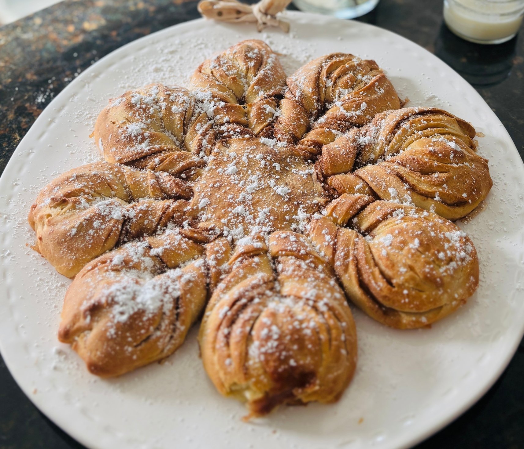 A white plate with star-shaped cinnamon buns dusted with powdered sugar on a dark surface.