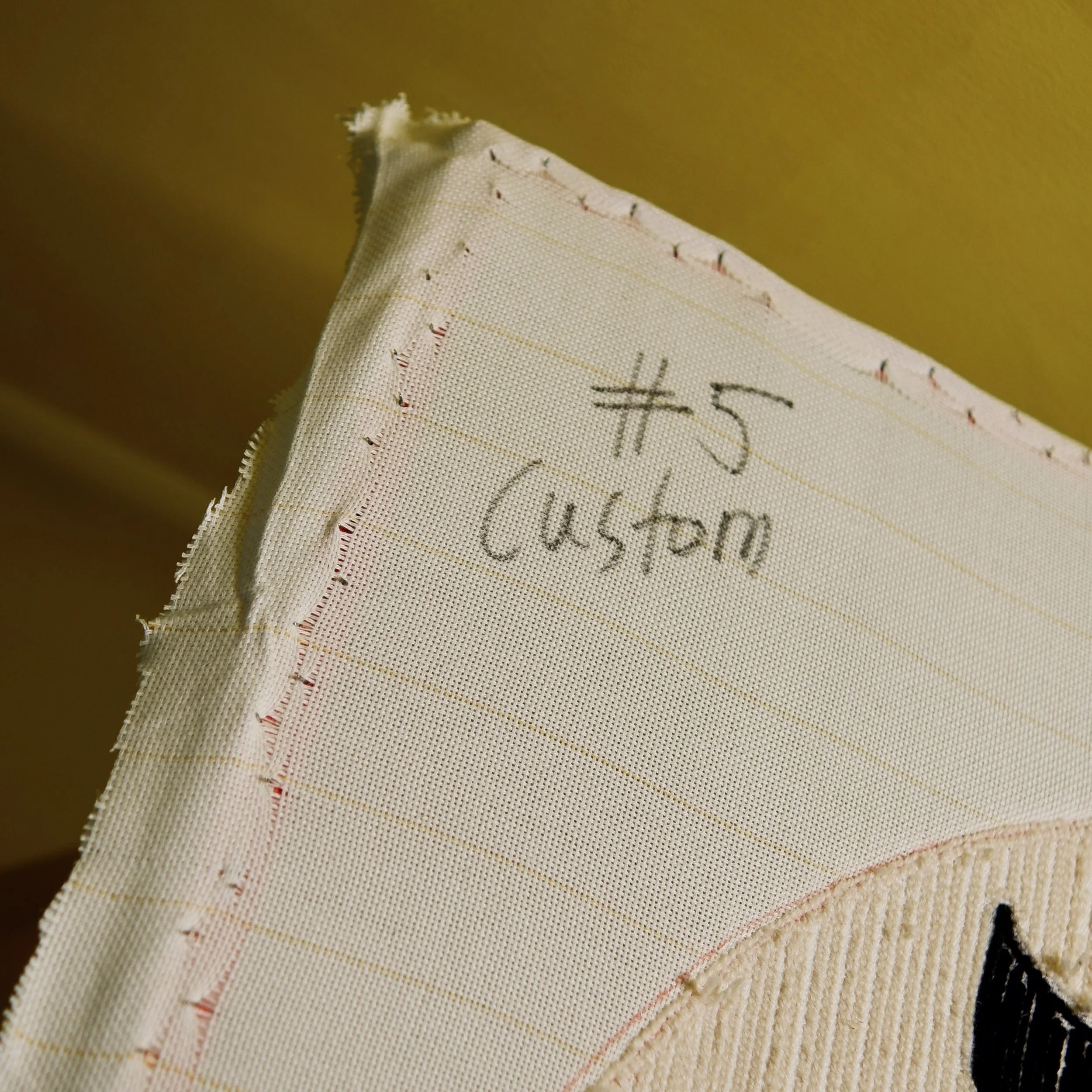 Close-up of a white fabric with a handwritten label '#5 Custom' stitched onto it.