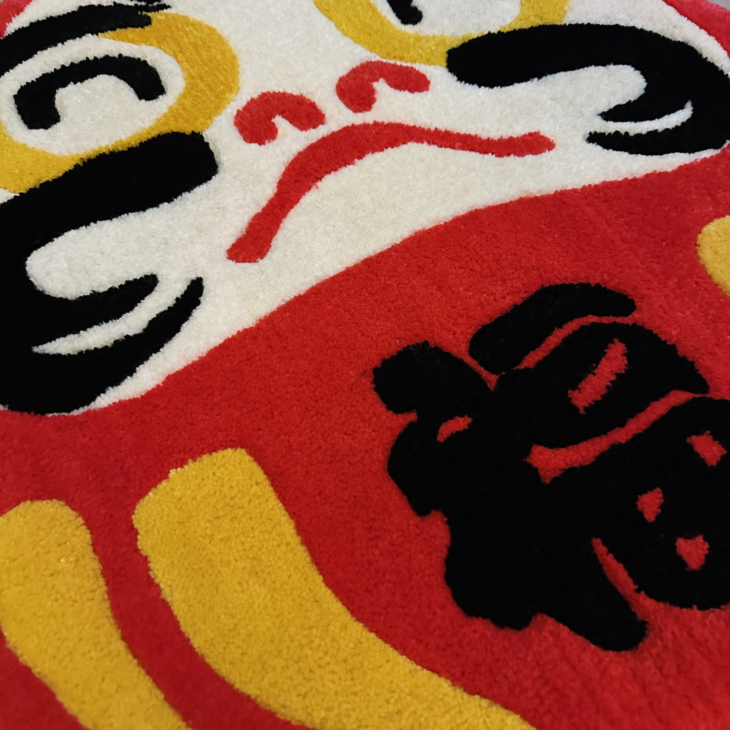 Close-up of a colorful, textured fabric featuring a graphic design Daruma, primarily in black, white, red, and yellow.