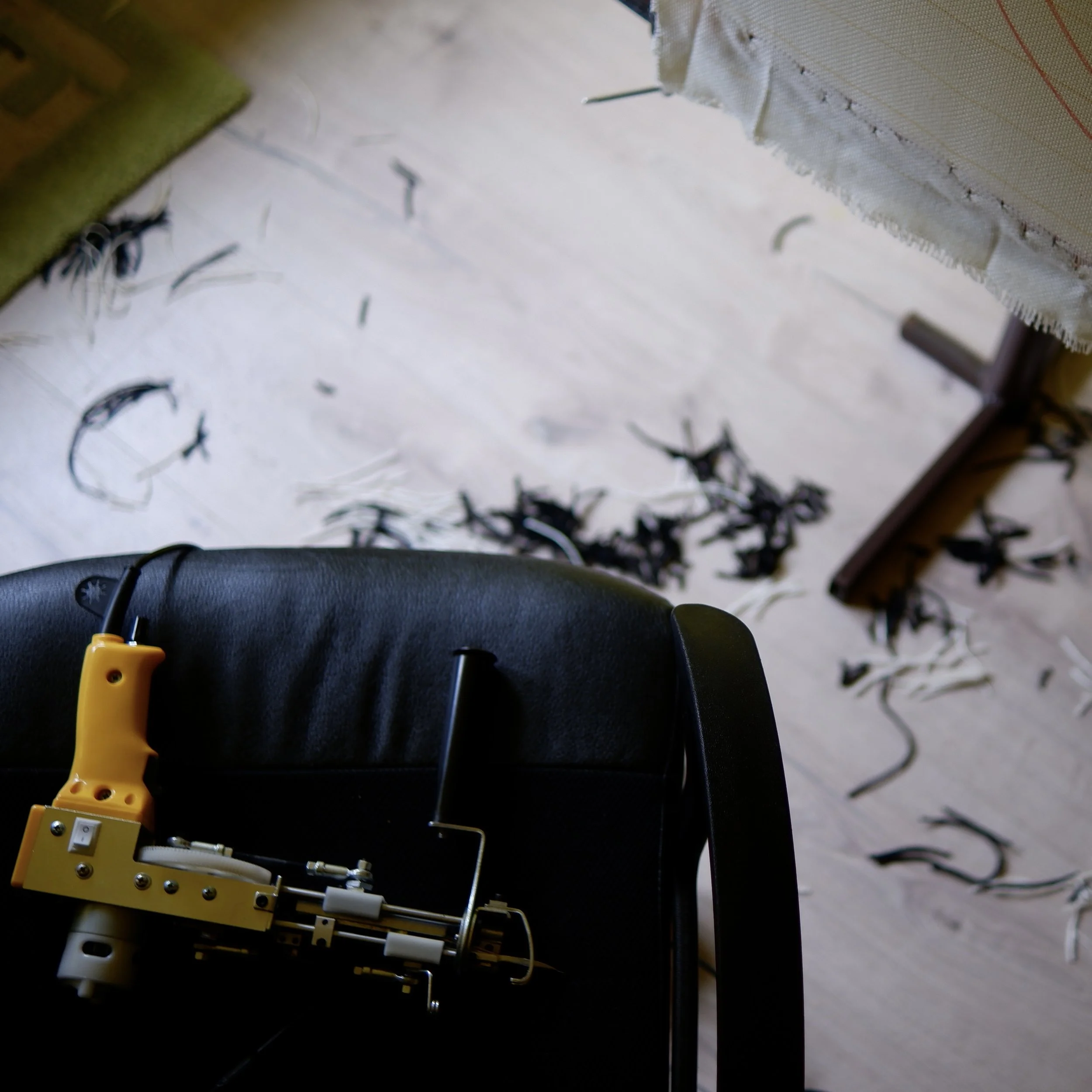 A chair with a latex bed of shredded paper and a embroidery machine on top, with scraps of black and white thread scattered on the floor.