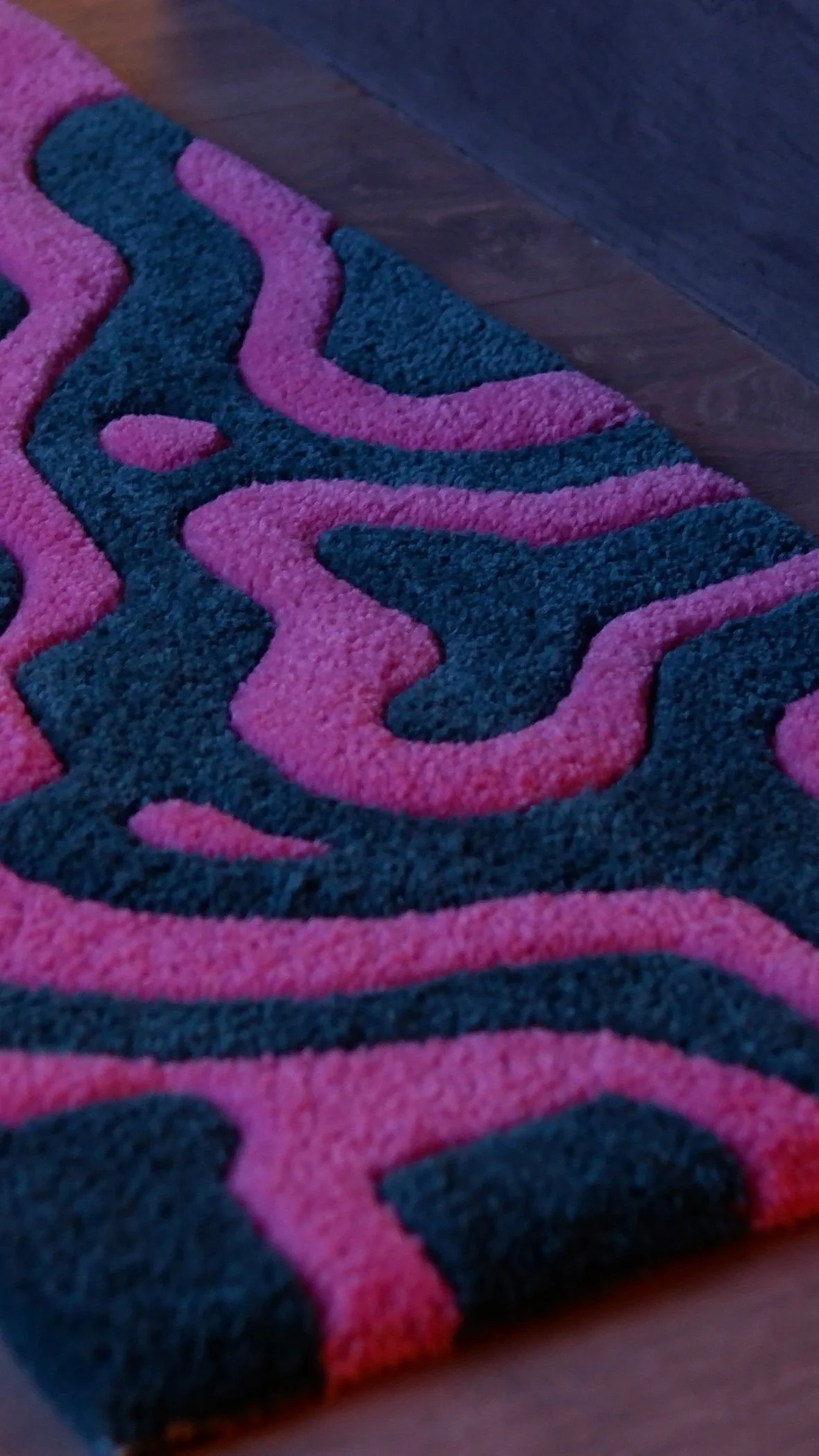 Close-up view of a multicolored, patterned area rug with pink and black swirled designs, placed on a dark wooden floor.