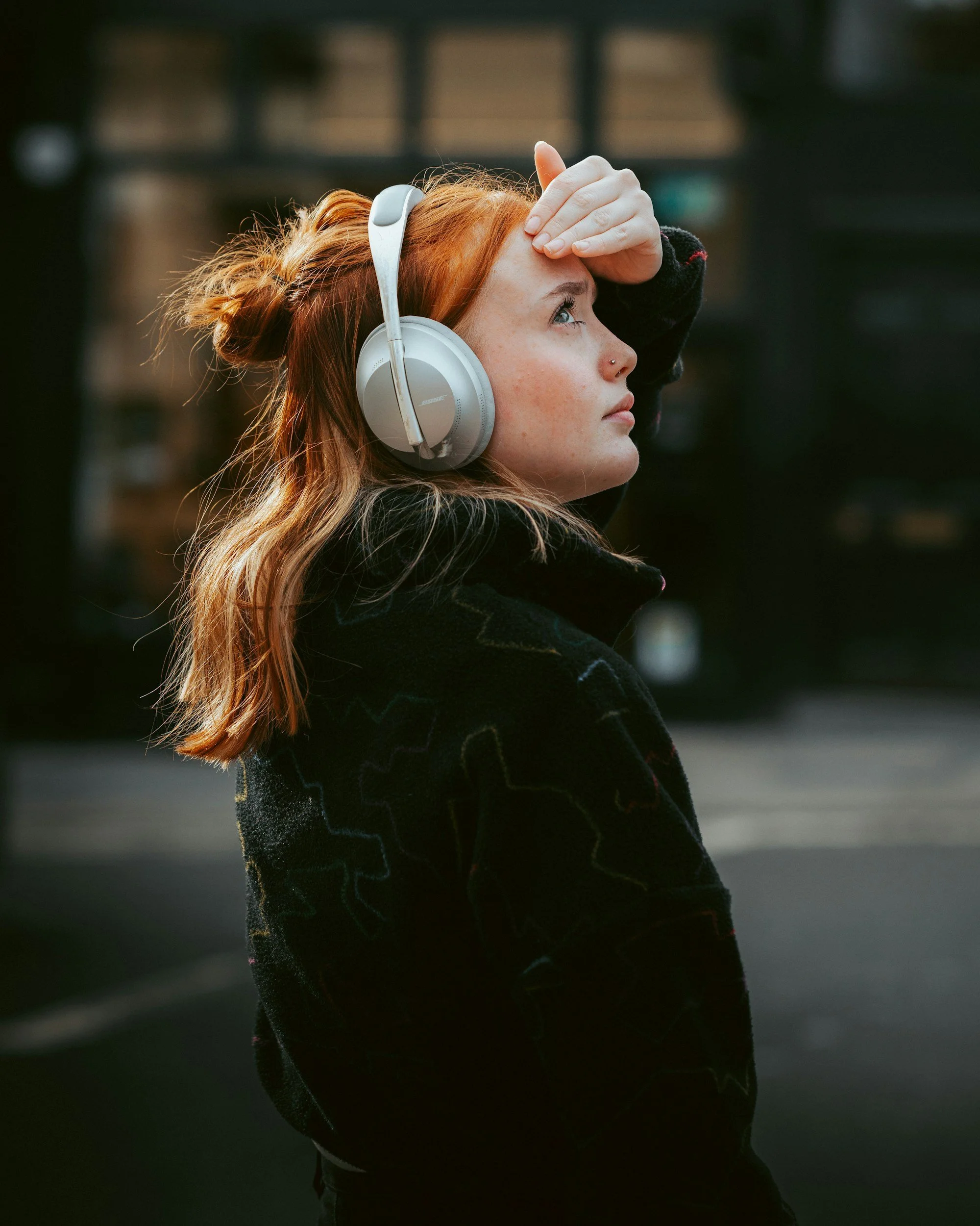 A person with red hair wearing white noise-canceling headphones outdoors; representing sensory processing needs and neuro-affirming therapy accommodations.