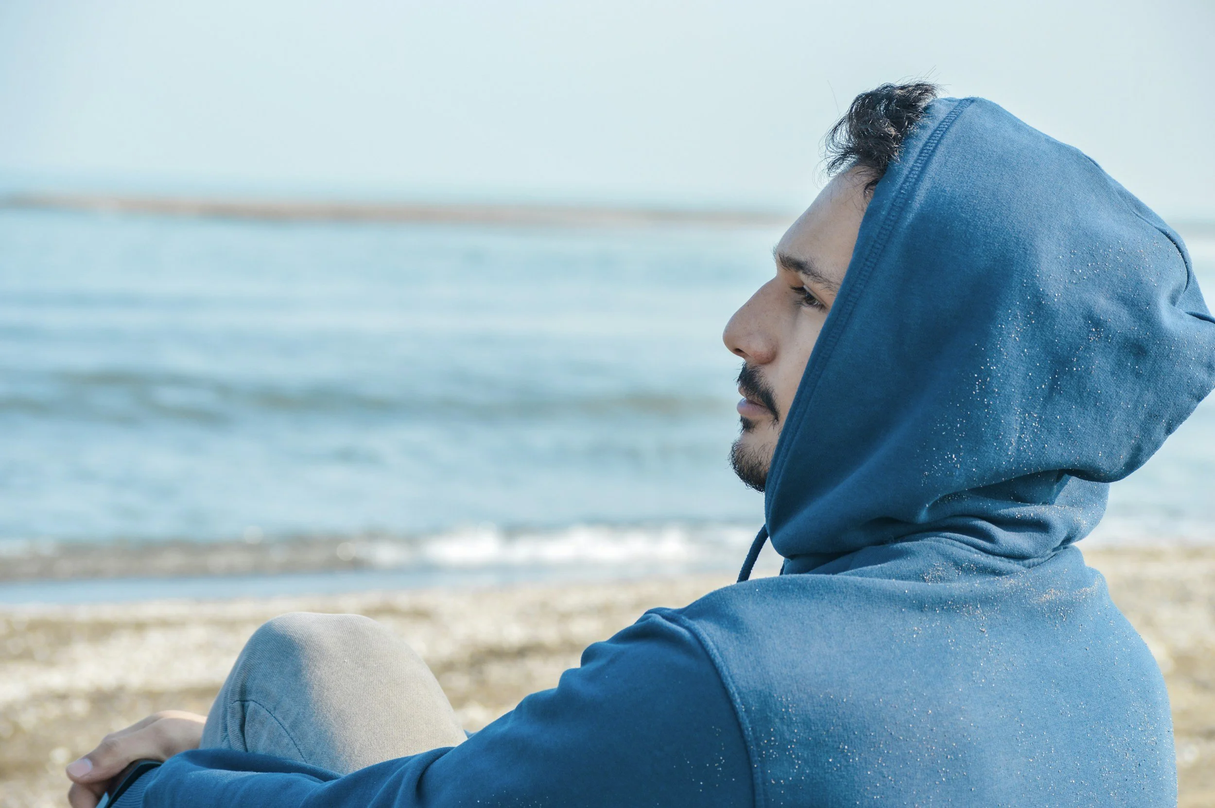 A person in a blue hoodie meditating on a beach; using grounding techniques to manage complex PTSD and dissociation.