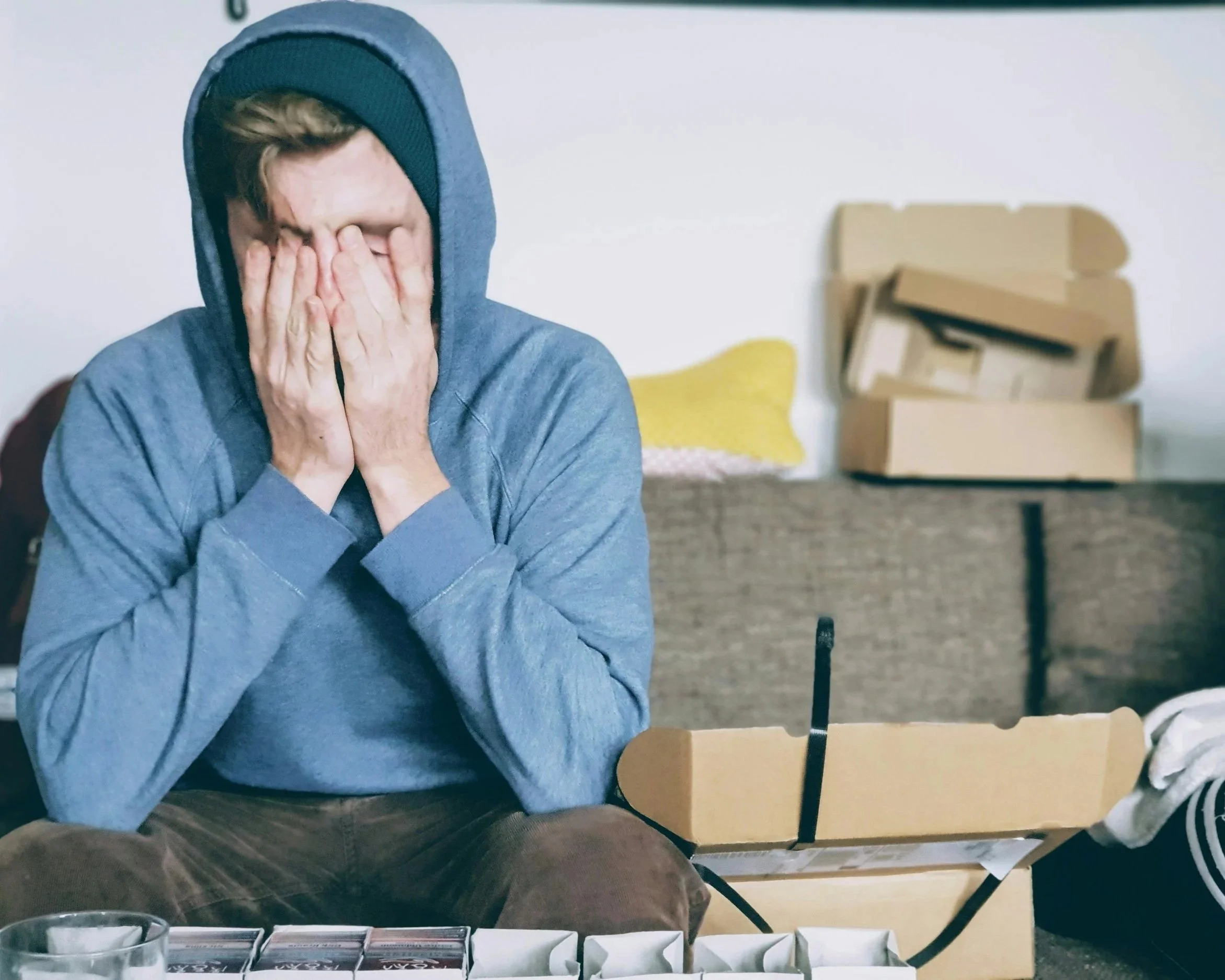 A person sitting with their face in their hands near moving boxes; illustrating the existential crisis and grief of institutional betrayal.