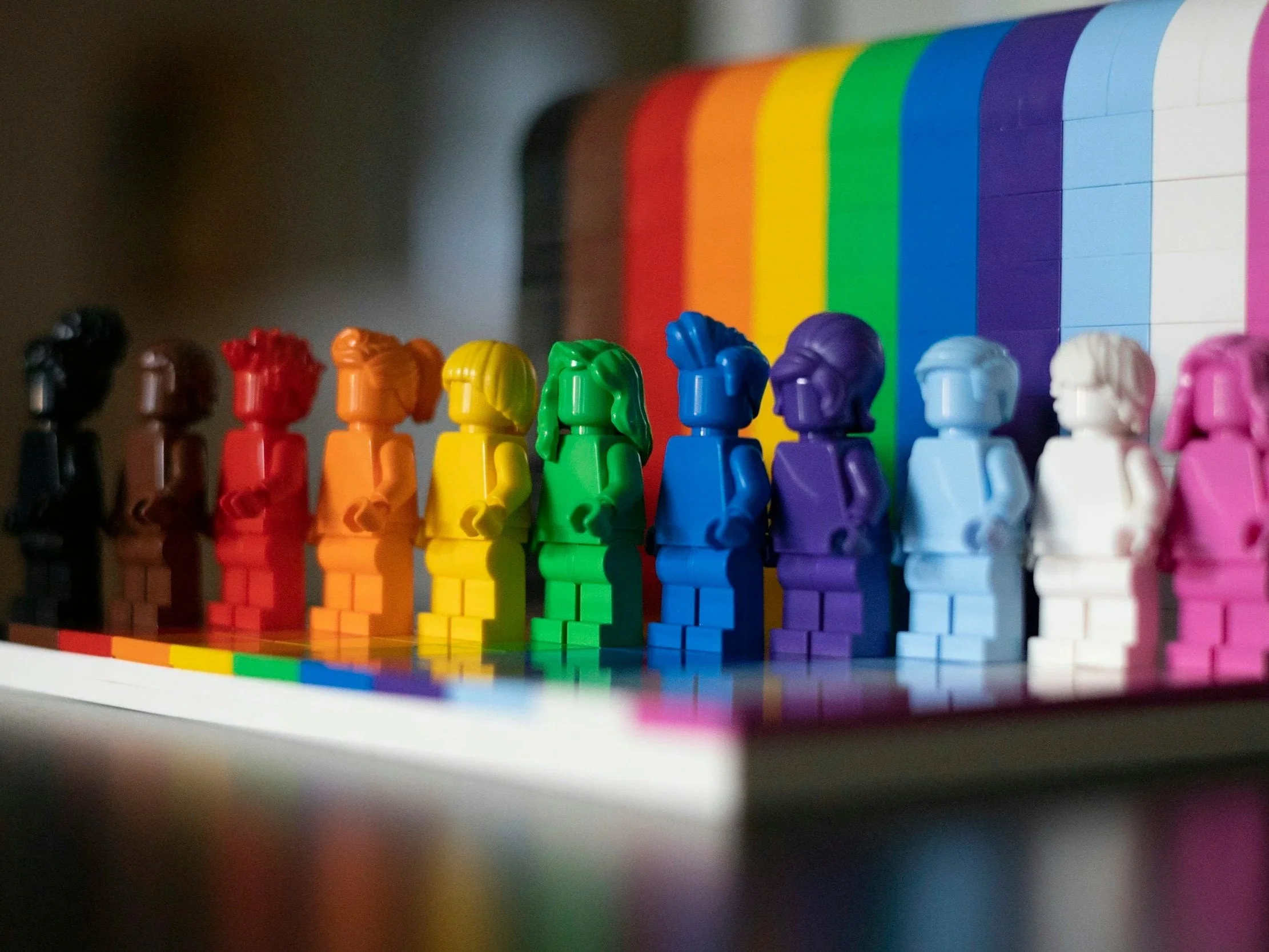 Colorful Lego figures lined up against a rainbow background; symbolizing inclusivity in trauma-informed mental health care.