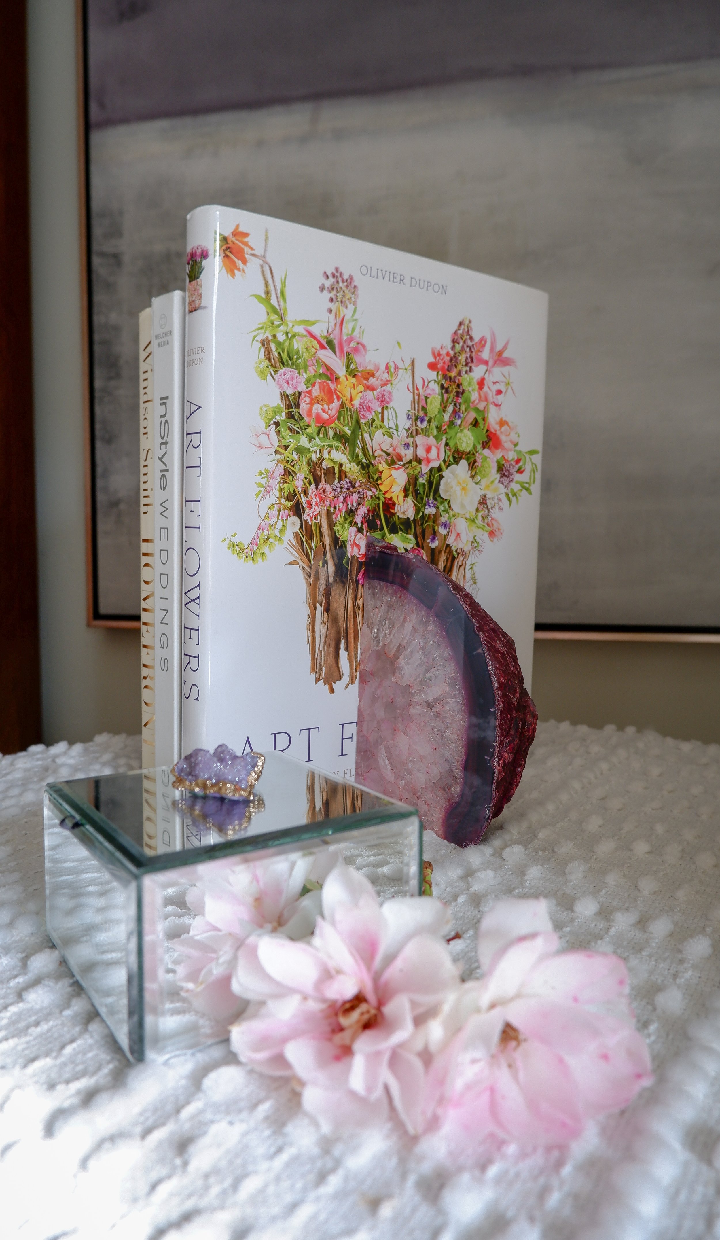Books with floral covers, glass cube with crystals, and pink flowers on a white textured surface.