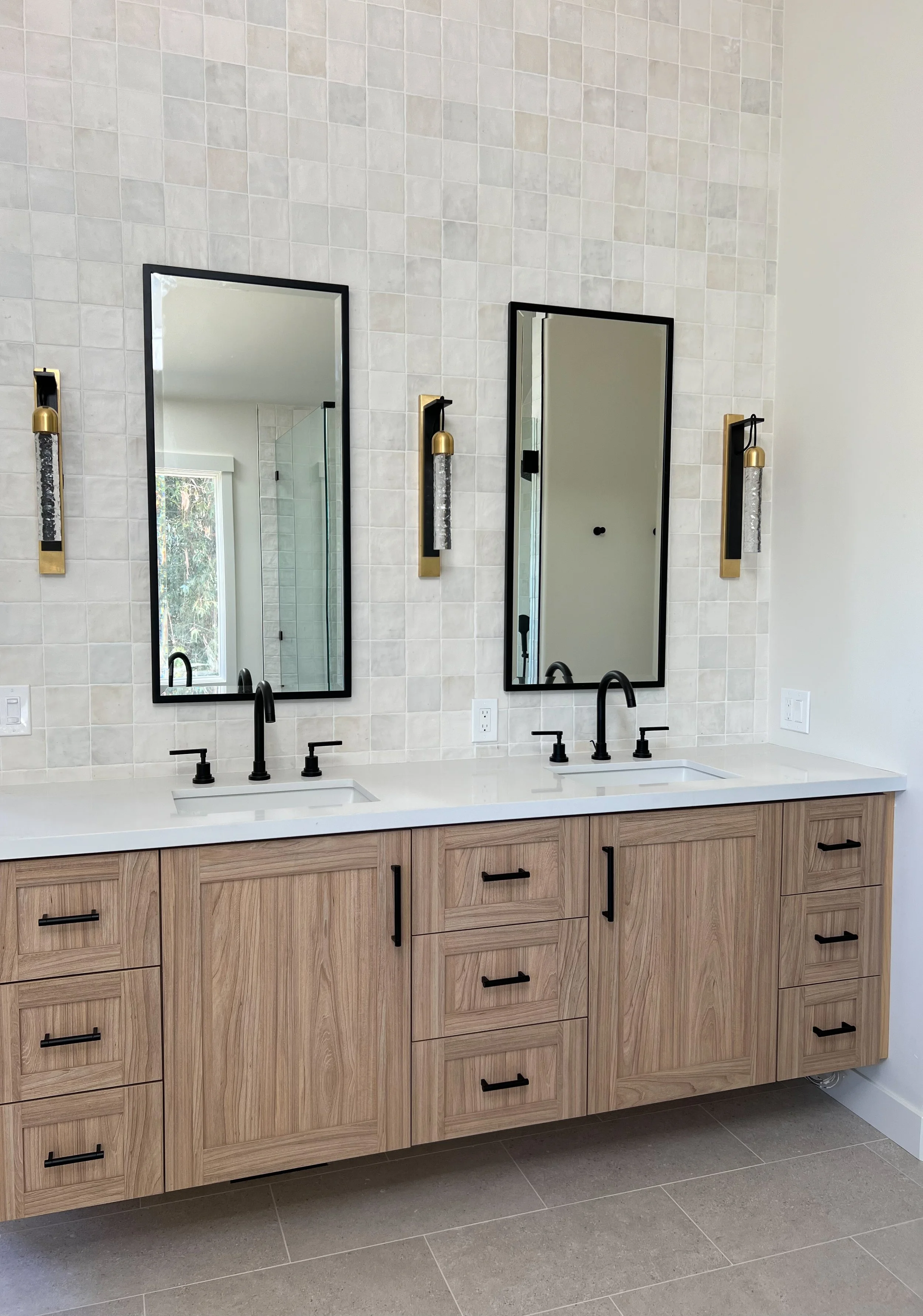 Modern bathroom with a double sink vanity, light wood cabinets, black hardware, white countertops, two rectangular mirrors, and wall sconces.