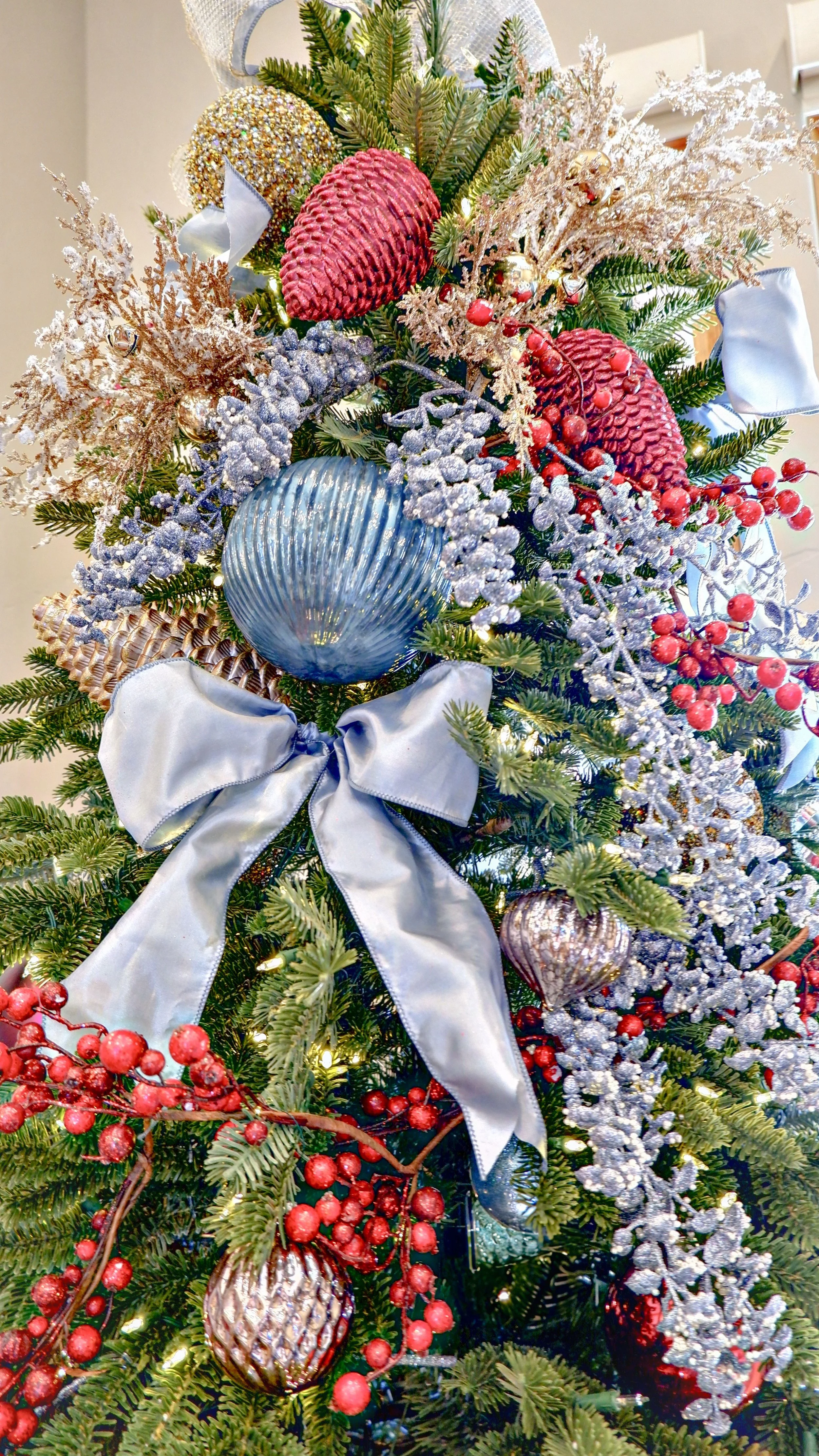 Christmas tree decorated with red and blue ornaments, silver and gold embellishments, and a large silver bow on top.