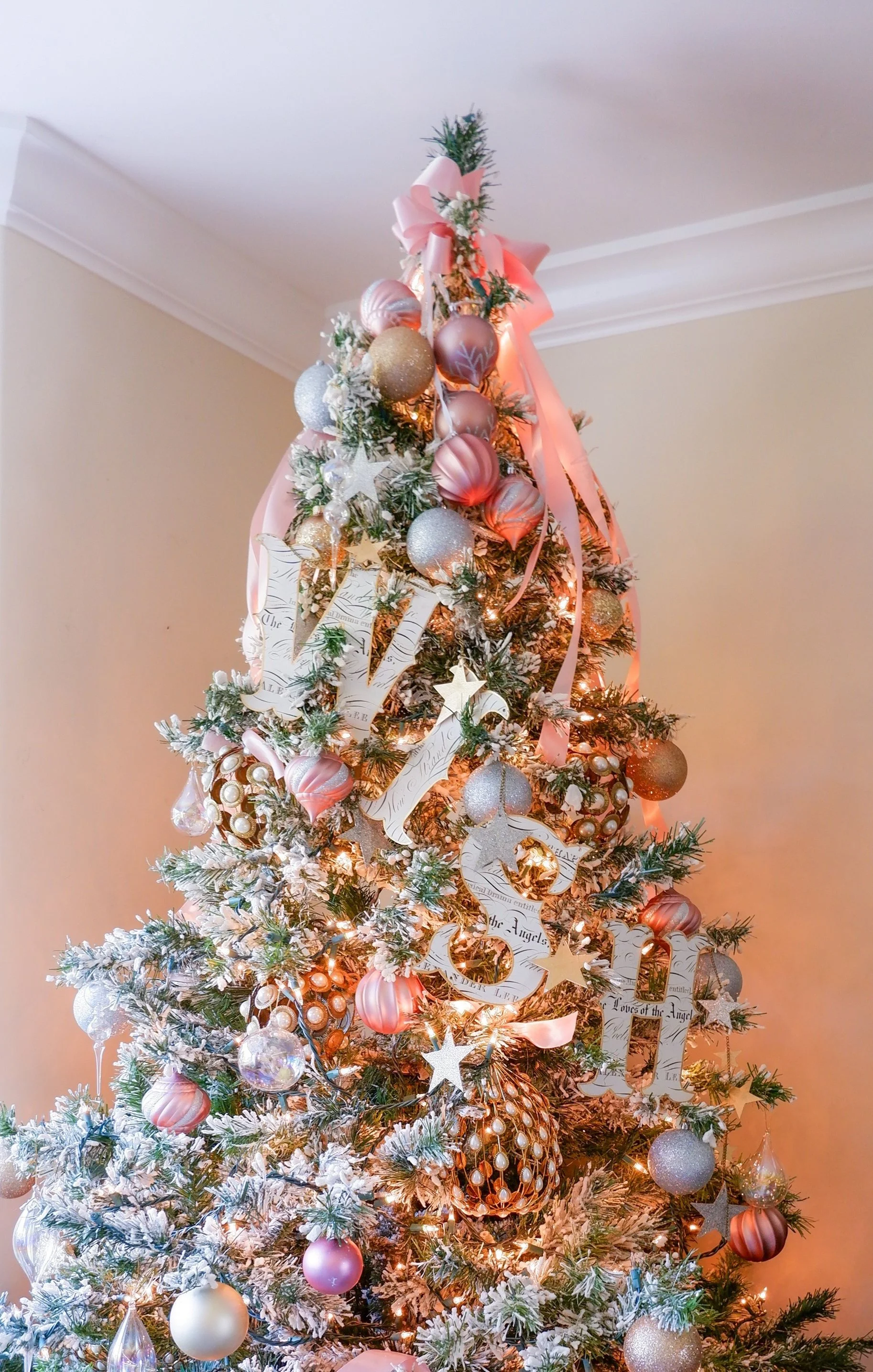 Christmas tree decorated with pink and gold ornaments, ribbons, and white lights.