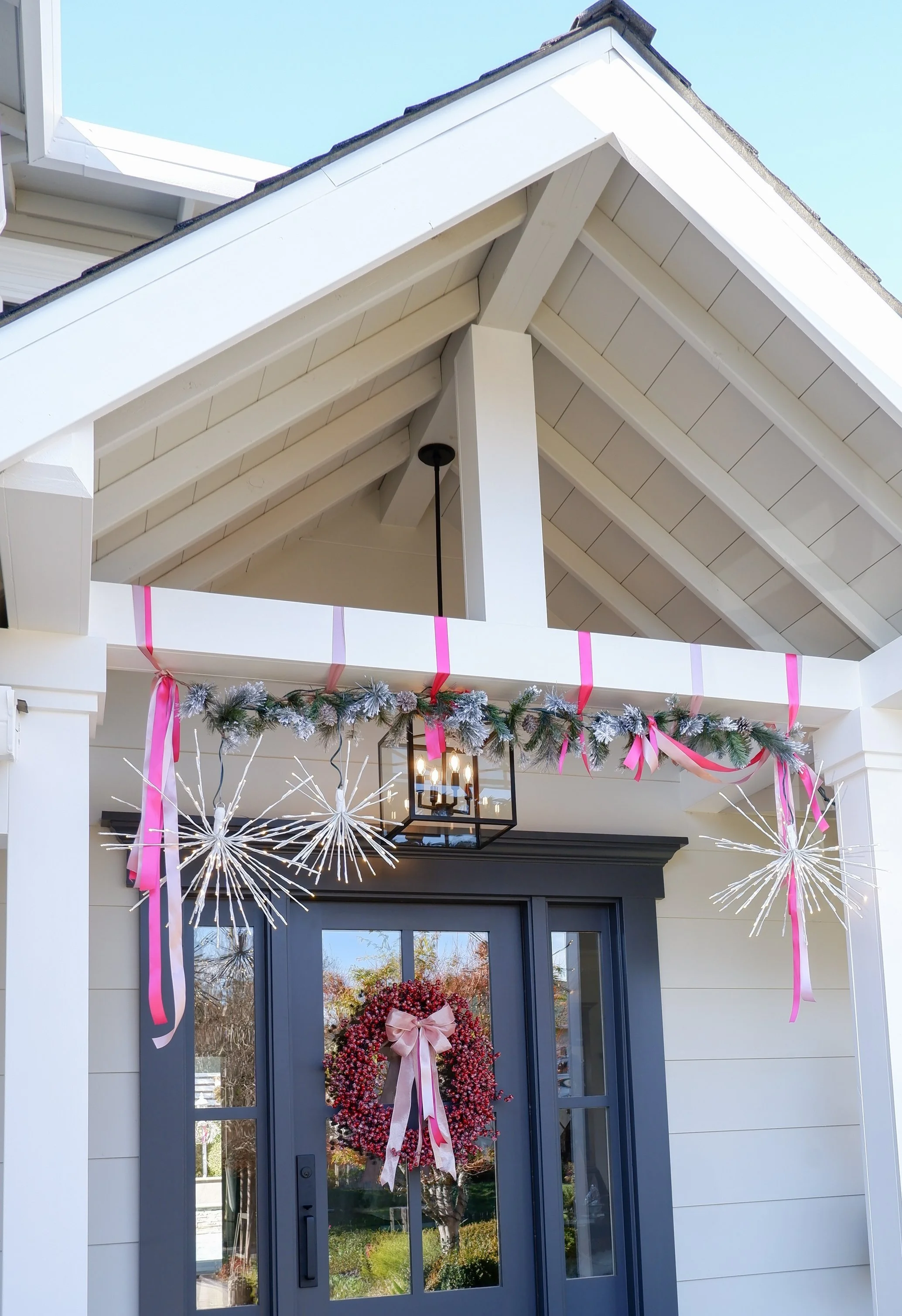 Decorated home entrance with garland, pink ribbons, wreath on door, and star-shaped decorations.
