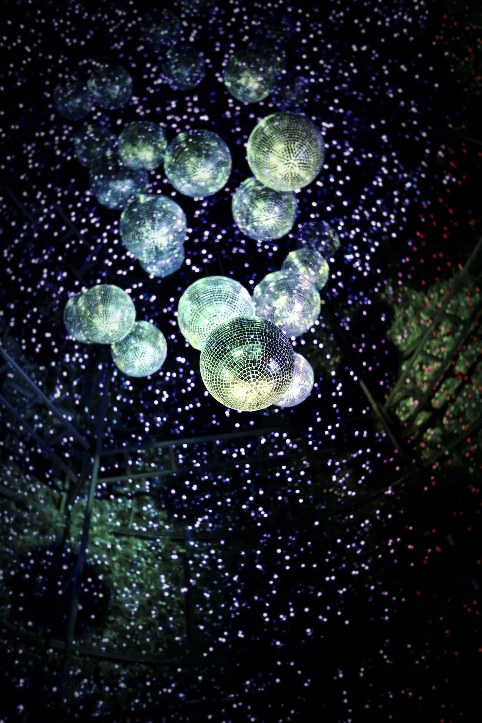 Several illuminated disco balls reflecting colorful lights in a dark space, creating a starry effect.