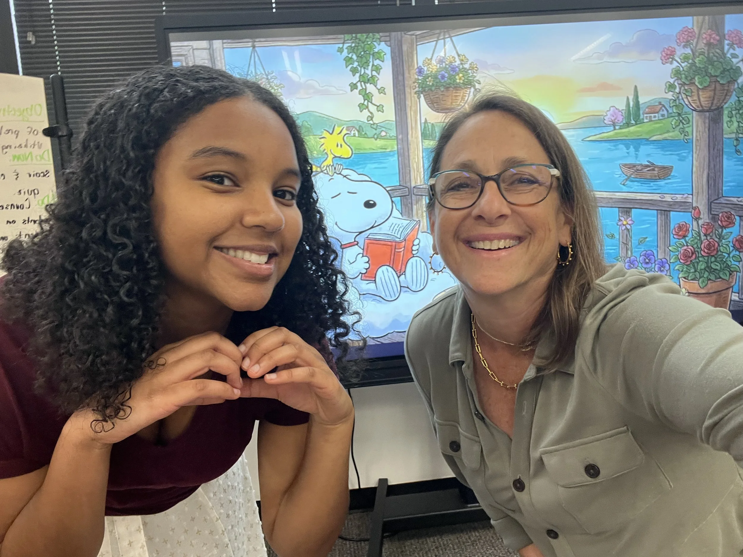 Debbie and a high school graduate mentee, taking a selfie, smiling at camera. Mentee is making a heart with her hands.