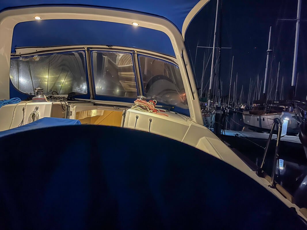 Interior view of a yacht with a covered cockpit at night in a marina, surrounded by other boats.