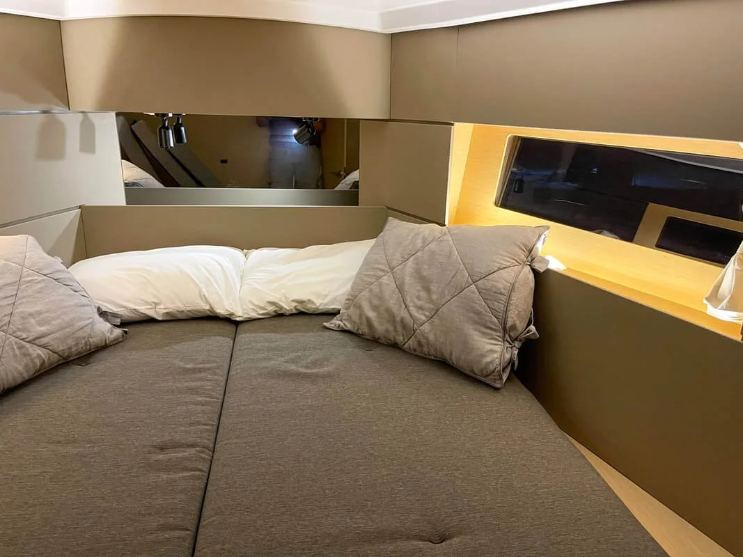 Cozy bedroom interior with a double bed, gray pillows, and brown headboard. A window on the right wall provides natural light.