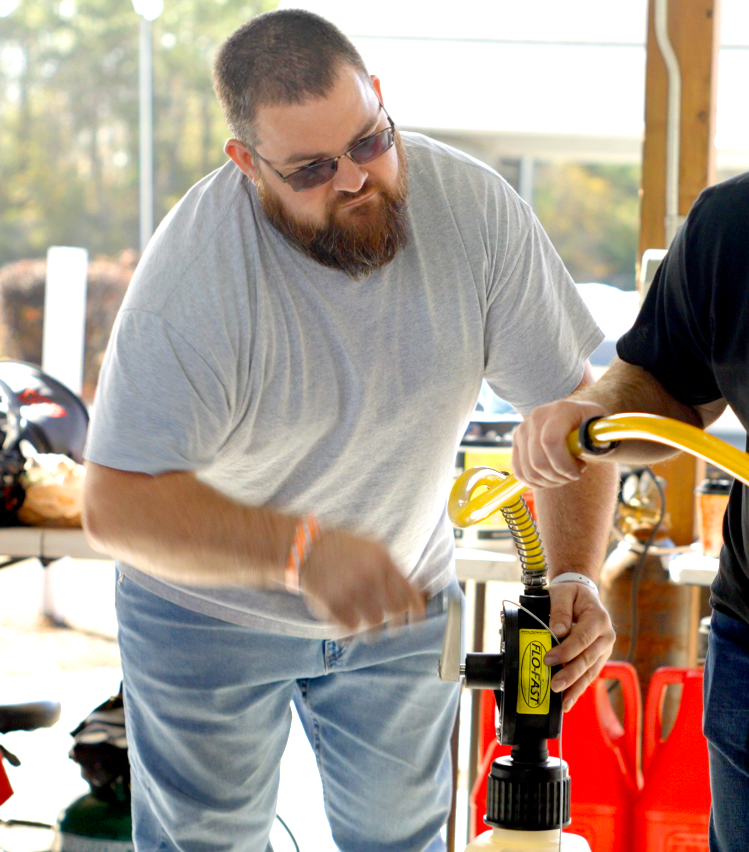 Pit Boss, Chris White wearing sunglasses and a gray t-shirt using a yellow and black pump on a yellow air compressor in a well-lit, outdoor setting.