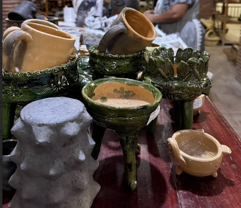 Various ceramic and pottery items on a red table, including mugs, planters, bowls, and a gray textured sculpture.