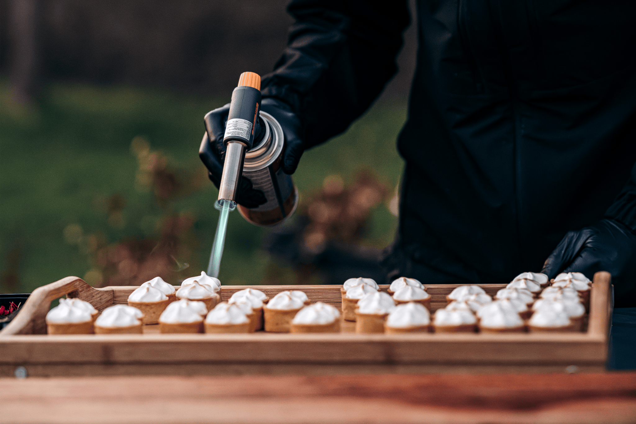 Persoon spuit slagroom op kleine koekjes die op een houten dienblad liggen, buiten.