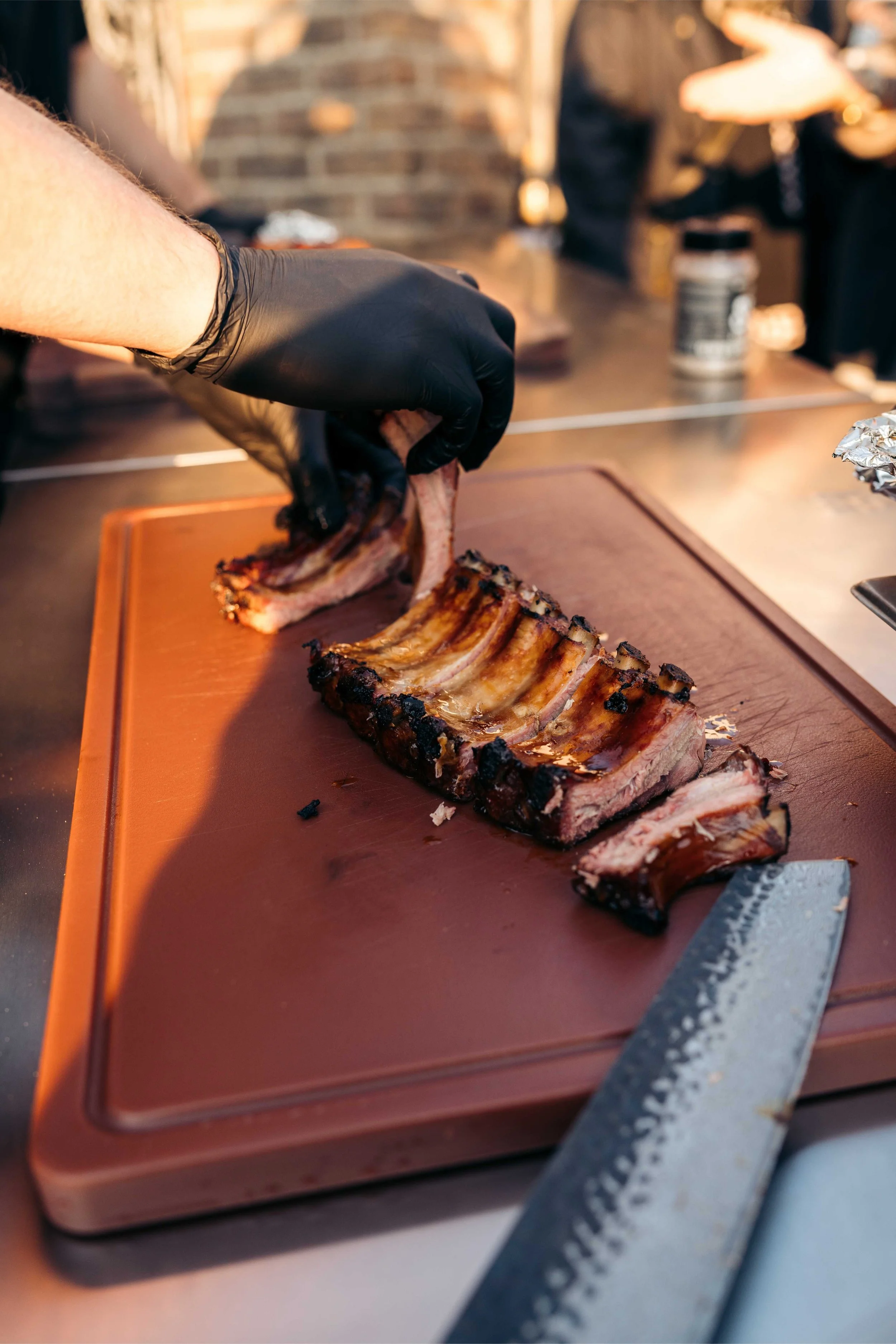 Persoon snijdt een geroosterde ribstuk op een snijplank. Een mes ligt naast de snijplank en er is een zwarte handschoen op de hand van de persoon.