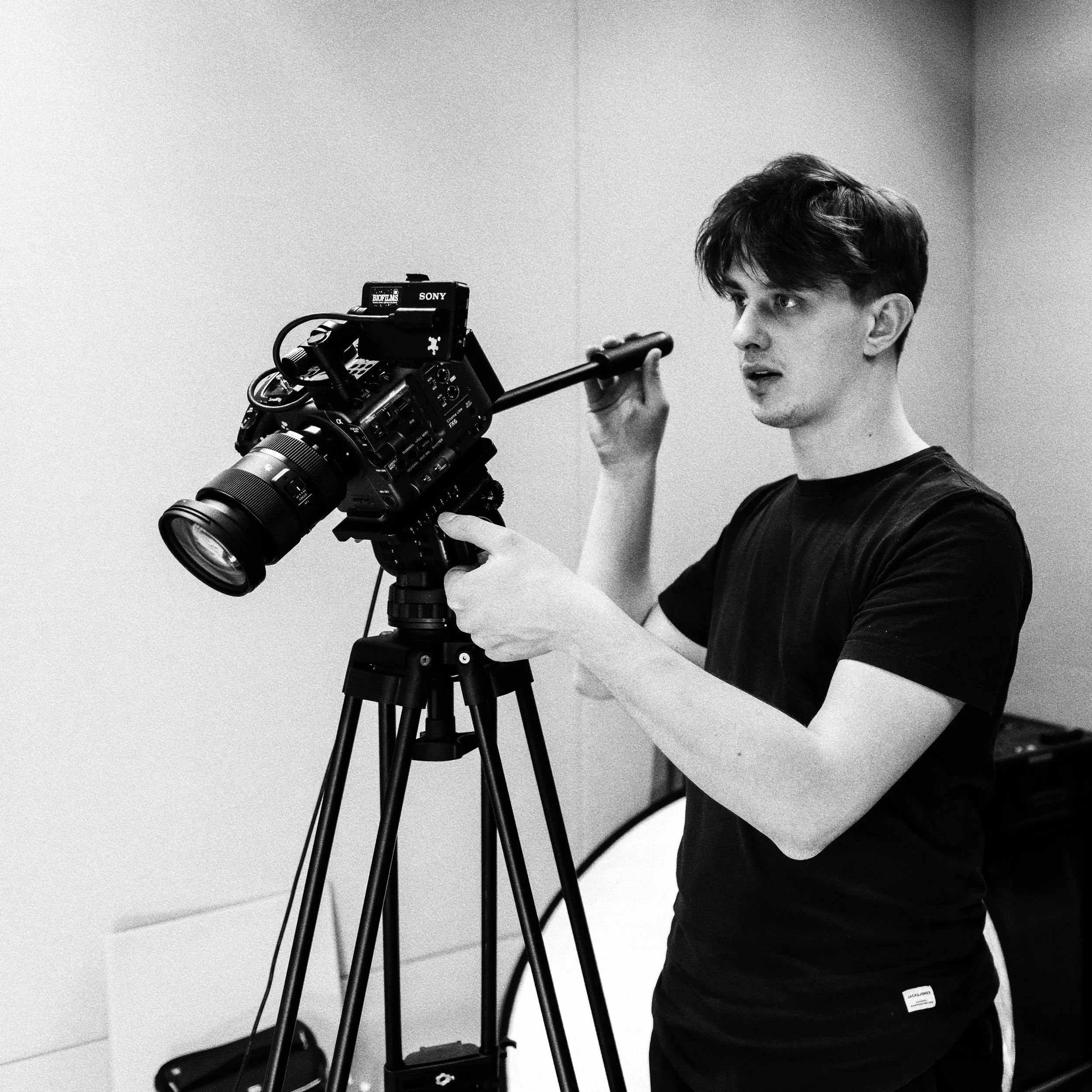 A young man adjusting a professional video camera on a tripod.