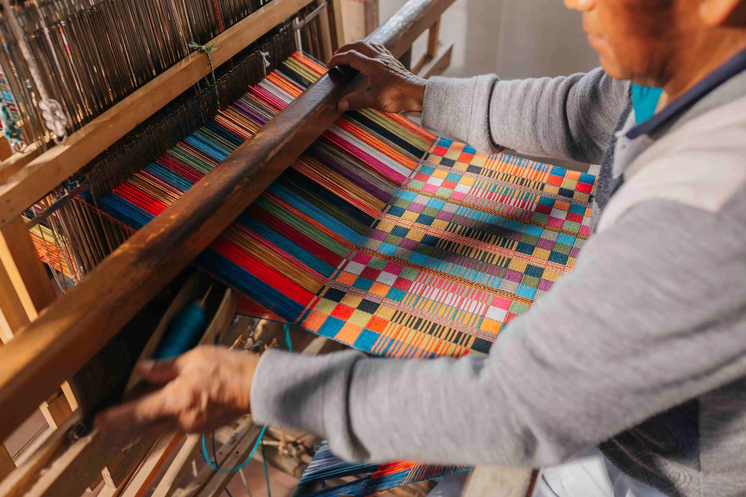 A person weaving a colorful patterned textile on a traditional loom.