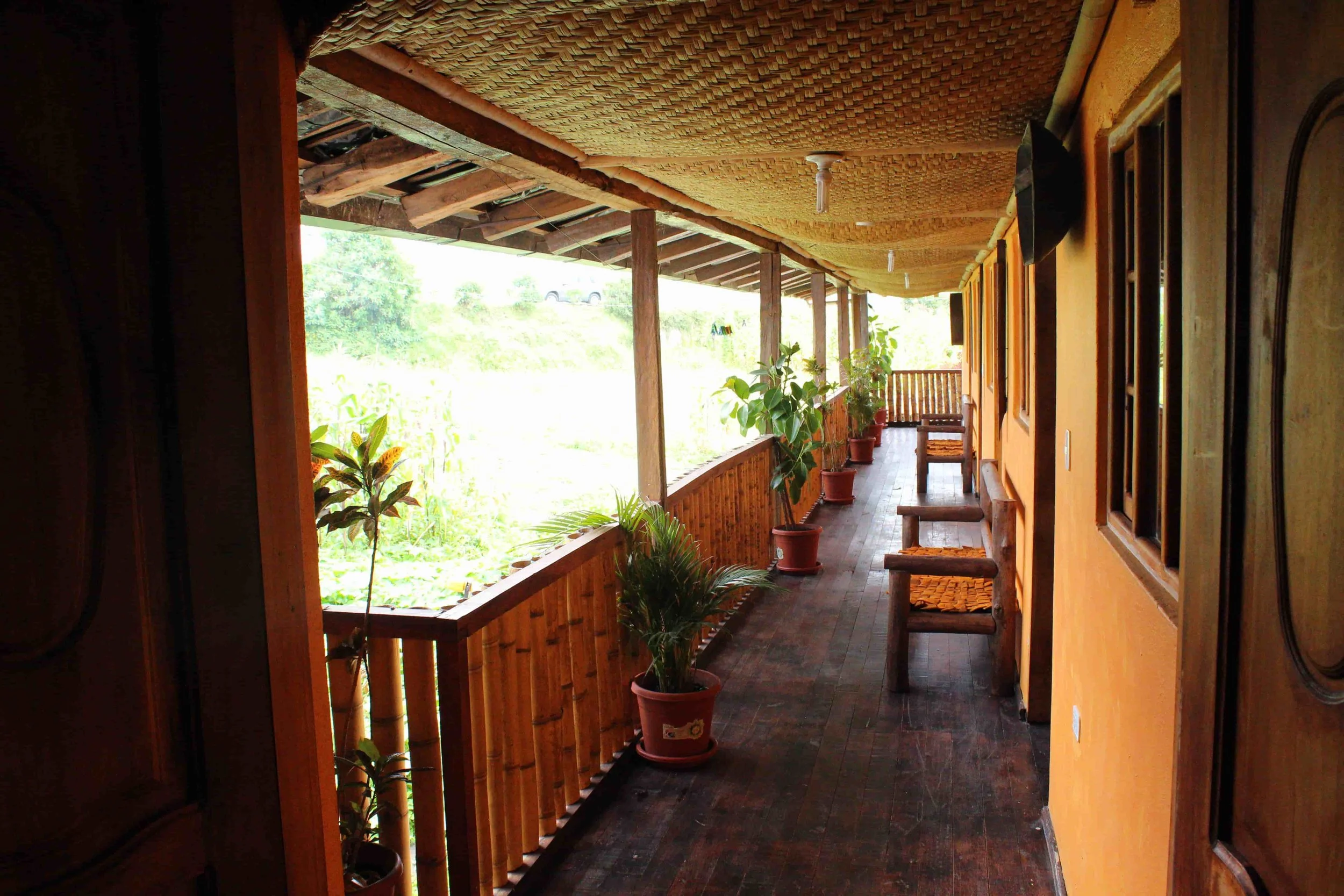 Covered porch with wooden railing, potted plants, and wooden benches overlooking greenery.
