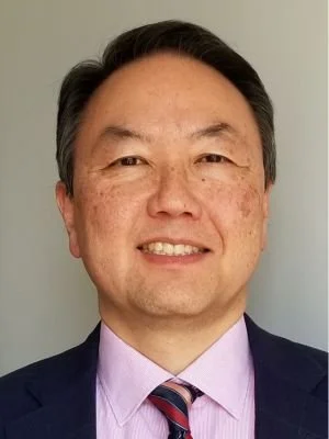 Close-up of a smiling man in a suit and tie against a plain background.
