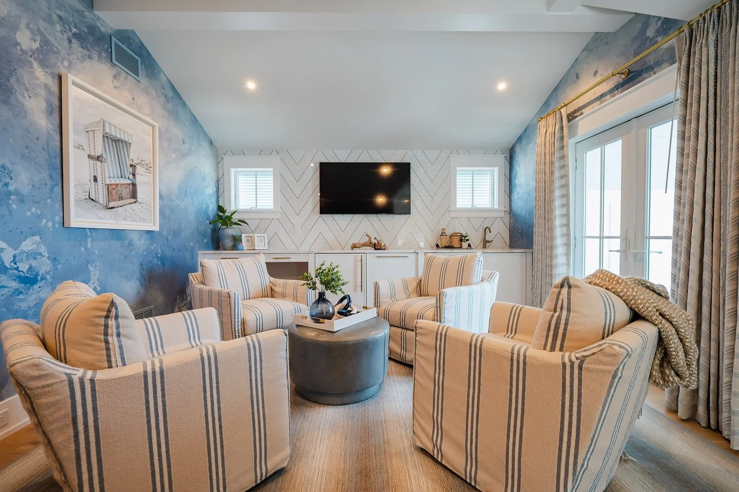 This lounge area proves that details make the space. Soft watercolor wallpaper brings the coastal feel while the herringbone tile adds just the right touch of polish. Stripes, texture, and coastal charm all in one cozy corner.