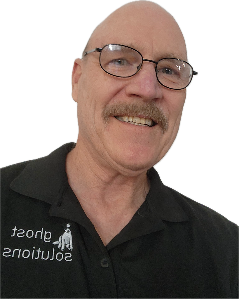 A smiling man with glasses and a mustache wearing a black shirt with a logo that says 'short solutions' and a small dog illustration.