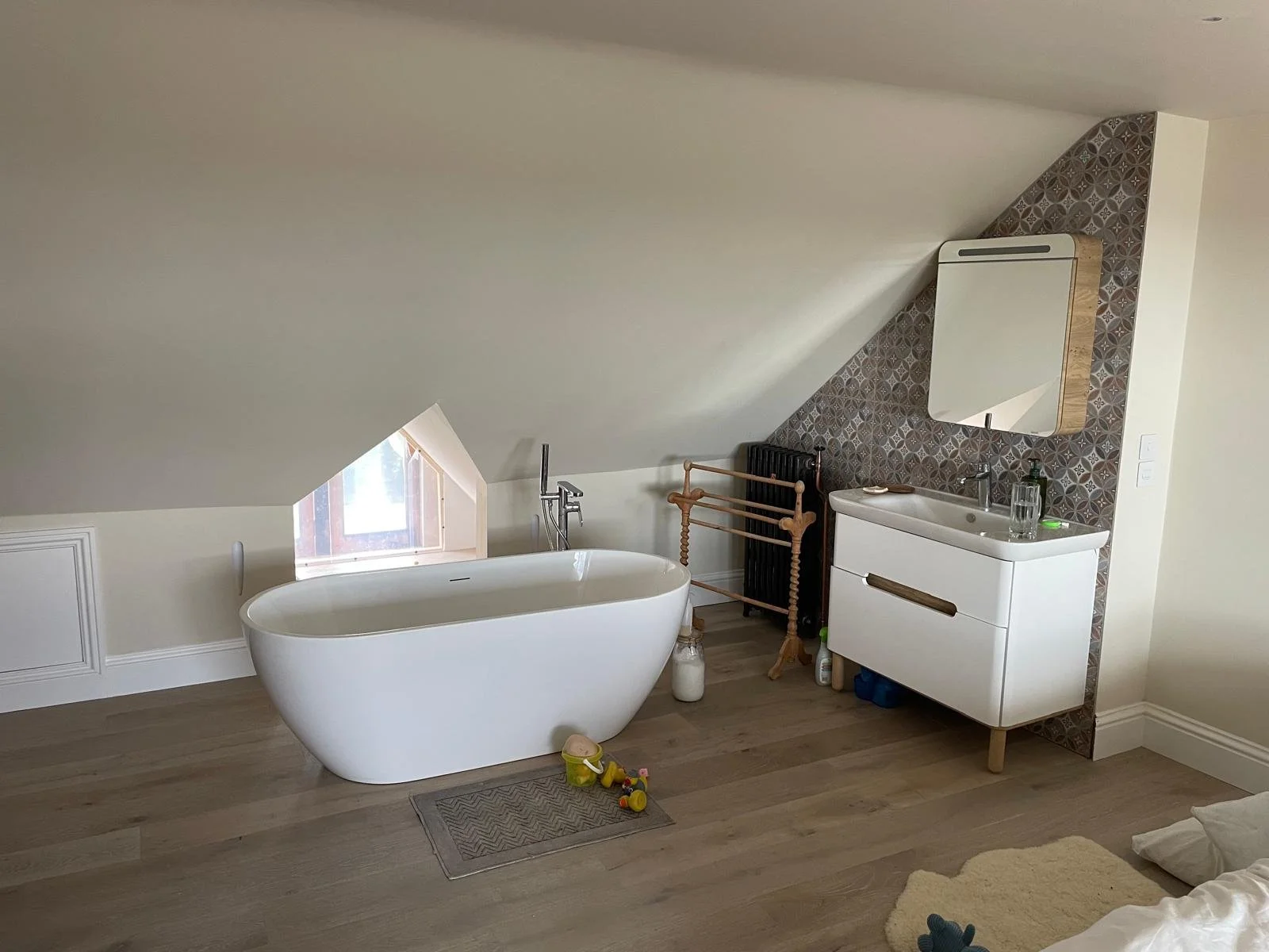 Bathroom with sloped ceiling, freestanding bathtub, small window, vanity with mirror, and children's toys on the floor.