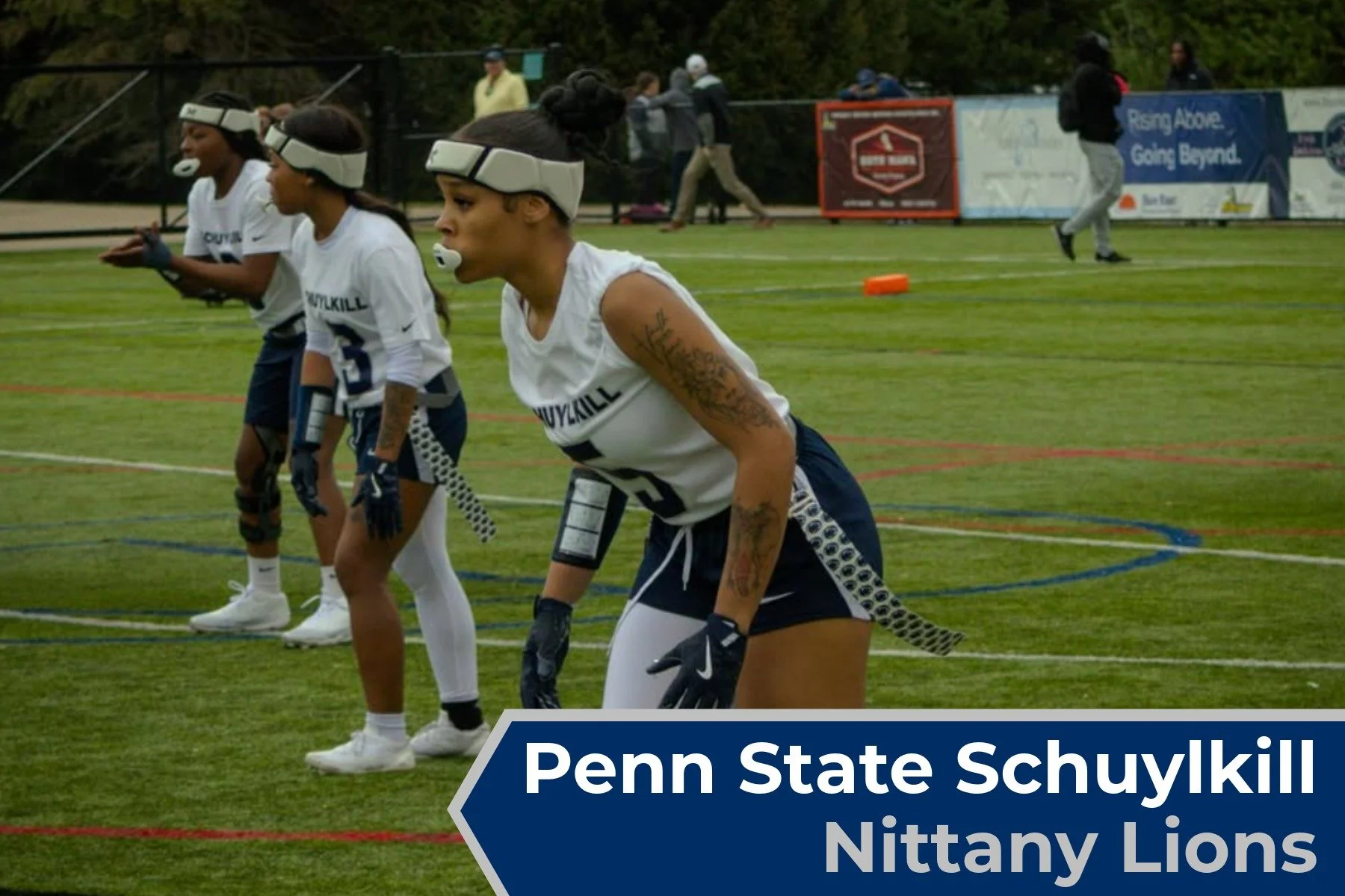 Four women in athletic gear on a sports field, preparing for a race with a banner in the background reading "Penn State Schuykill Nittany Lions."