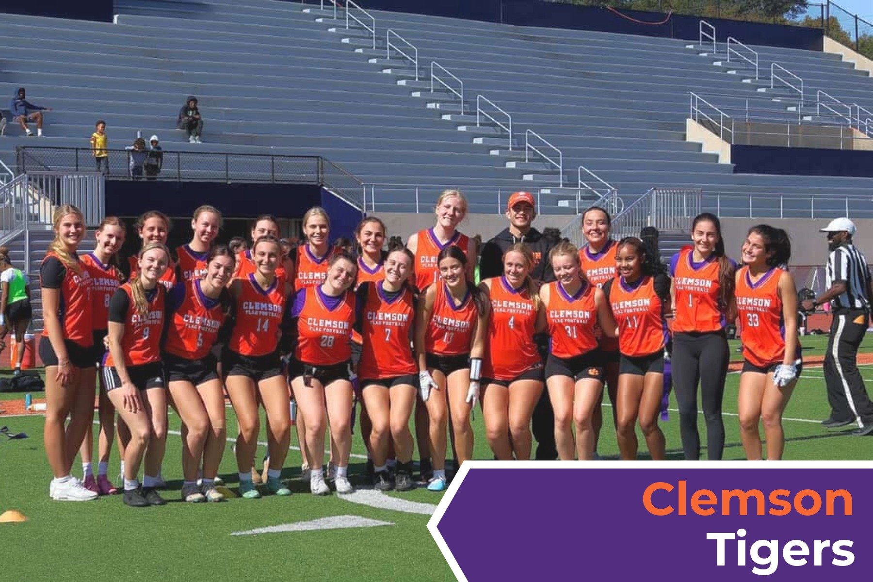 A group of female athletes in orange and black Clemson Tigers softball uniforms standing on a sports field with stadium seating behind them. They are smiling and posing for a team photo.