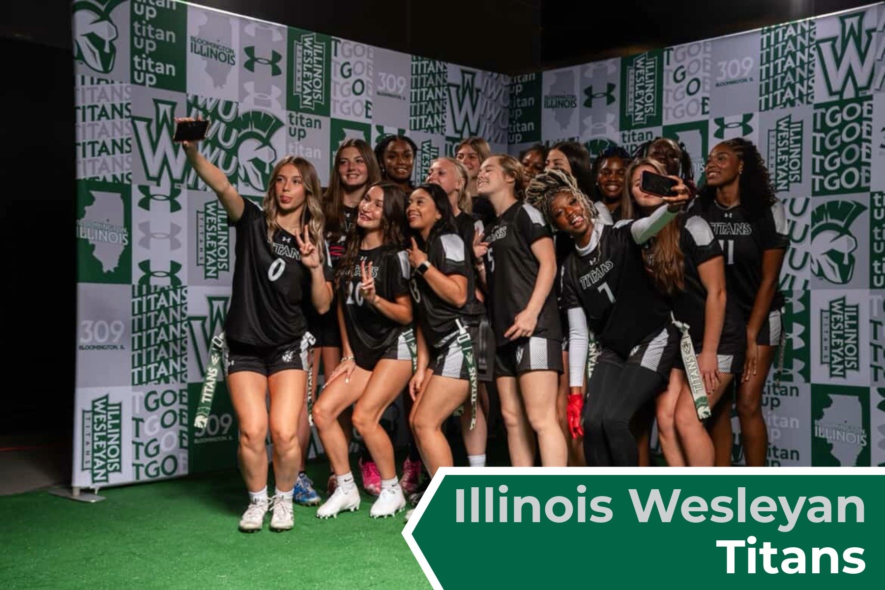 A team of female  Illinois Wesleyan Titans women's college flag football players taking a selfie on a green and white branded backdrop, wearing black and white sports uniforms.