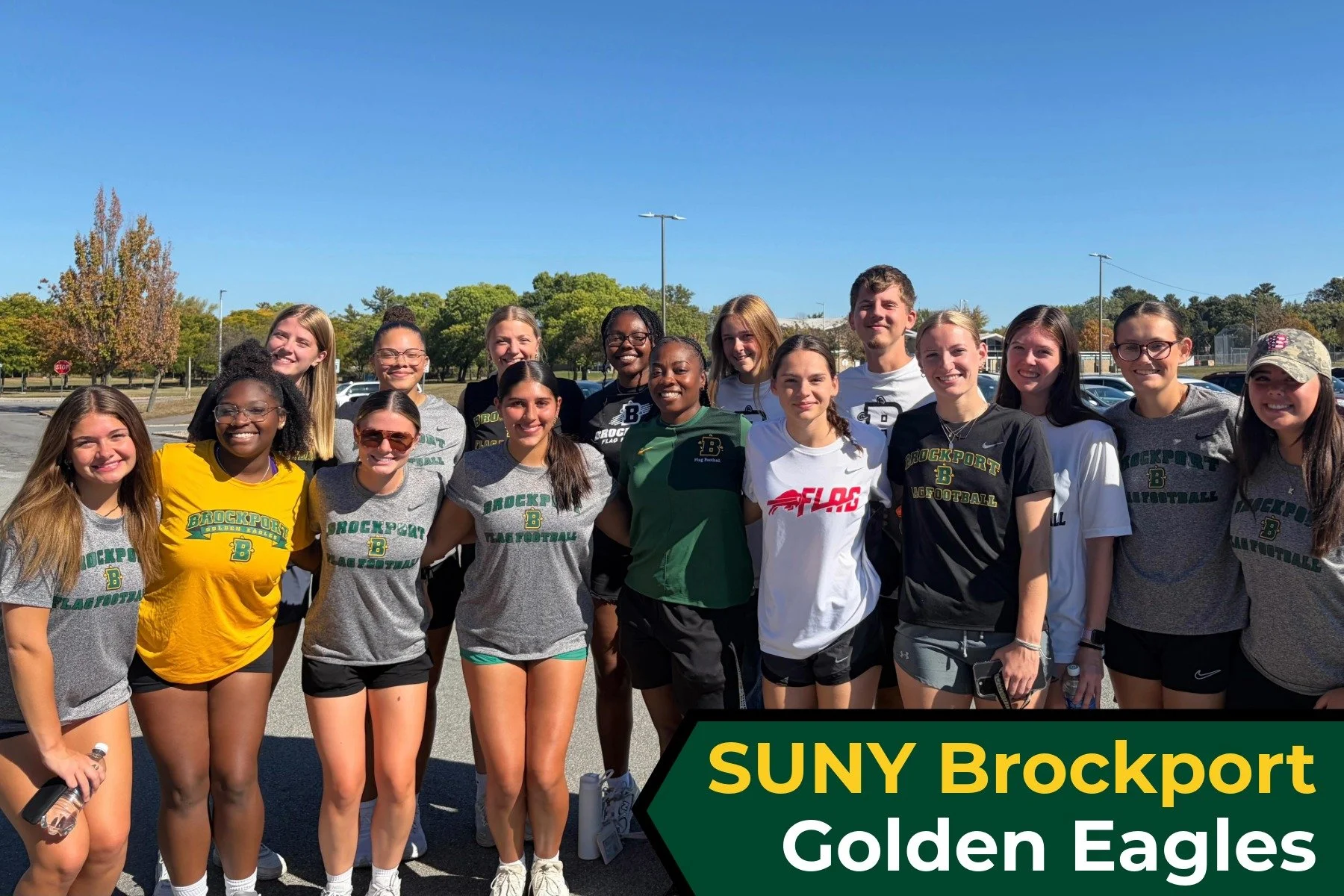 Group of young women and men standing outdoors on a sunny day in a parking lot with trees and blue sky in the background. They are wearing athletic clothing, some with "Brockport" and "Flag Football" logos, smiling at the camera. A banner in the bott