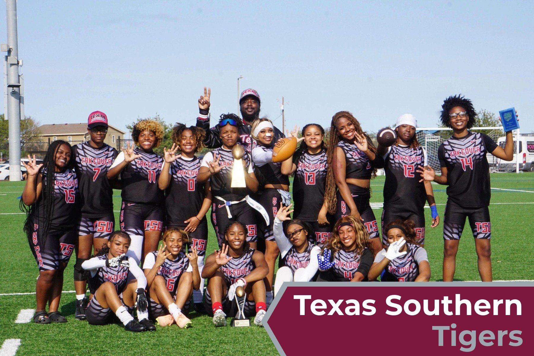 The Texas Southern Tigers girls' football team posing for a group photo on a football field, holding a trophy and footballs, wearing black and pink uniforms.