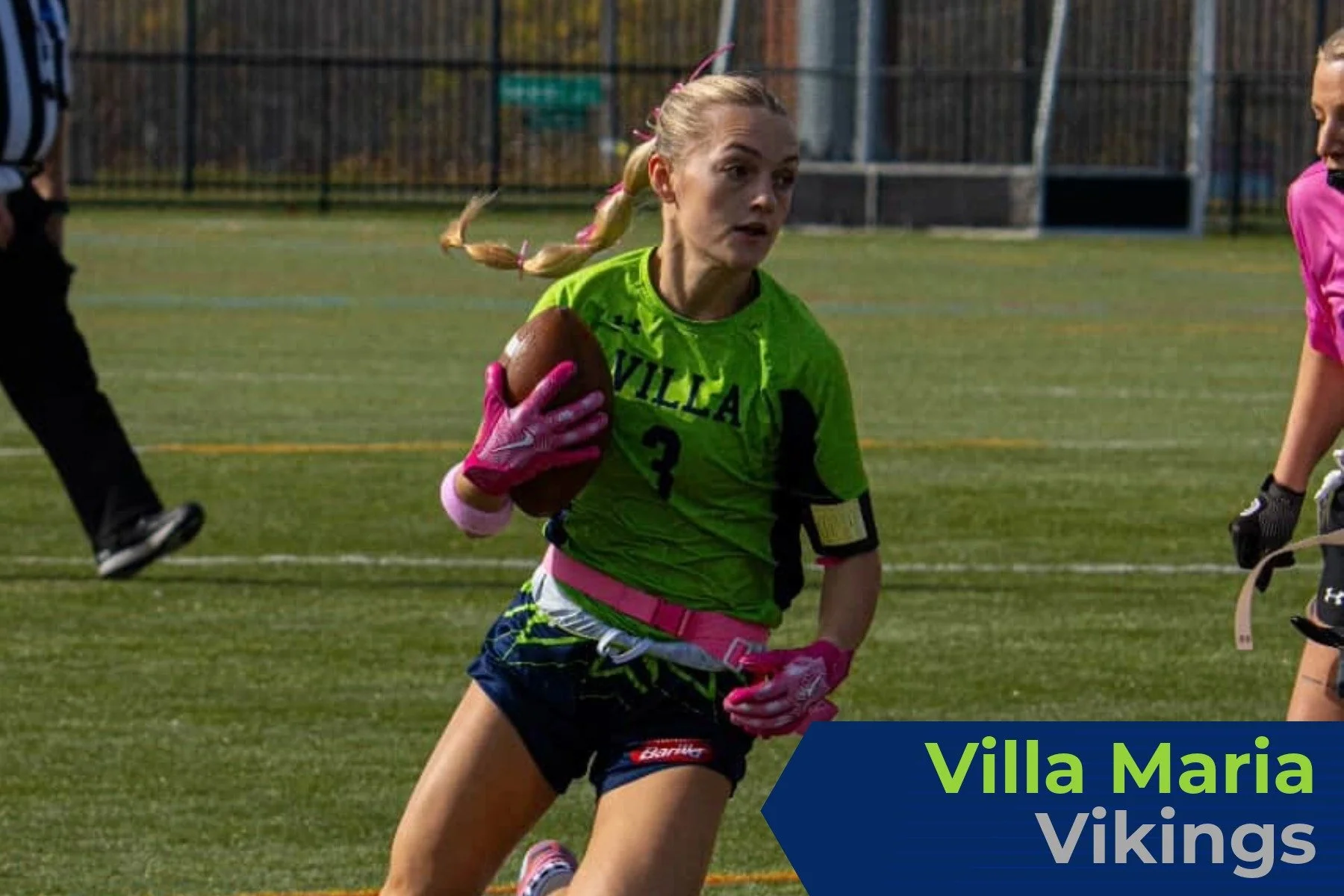 A female football player in a green and pink uniform with the number 3, running on a field with a football in her left arm during a game, with the words "Villa Maria Vikings" in the lower right corner.
