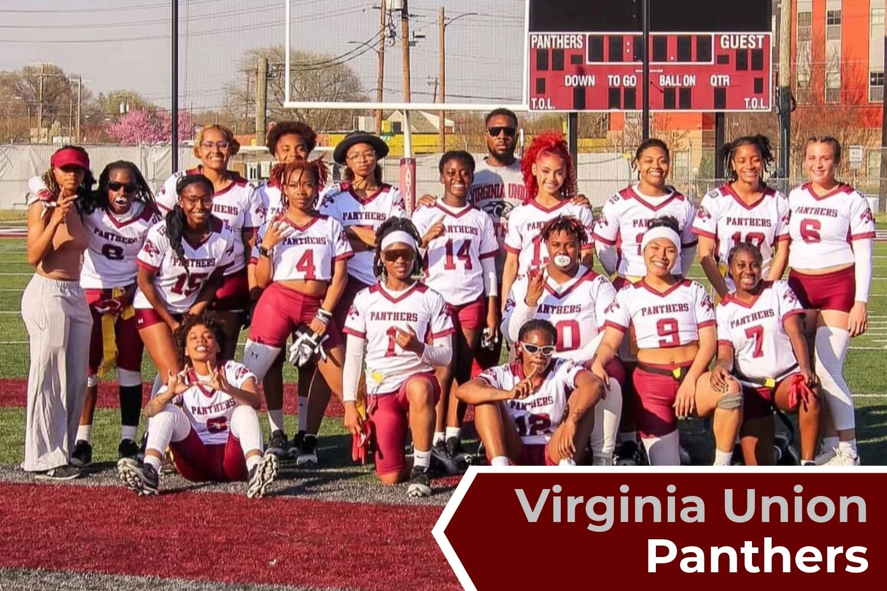 A women's football team called Virginia Union Panthers posing for a team photo on a football field. The team members are wearing white and maroon football jerseys with the team's name. Some are kneeling, some standing, with a scoreboard and trees in 
