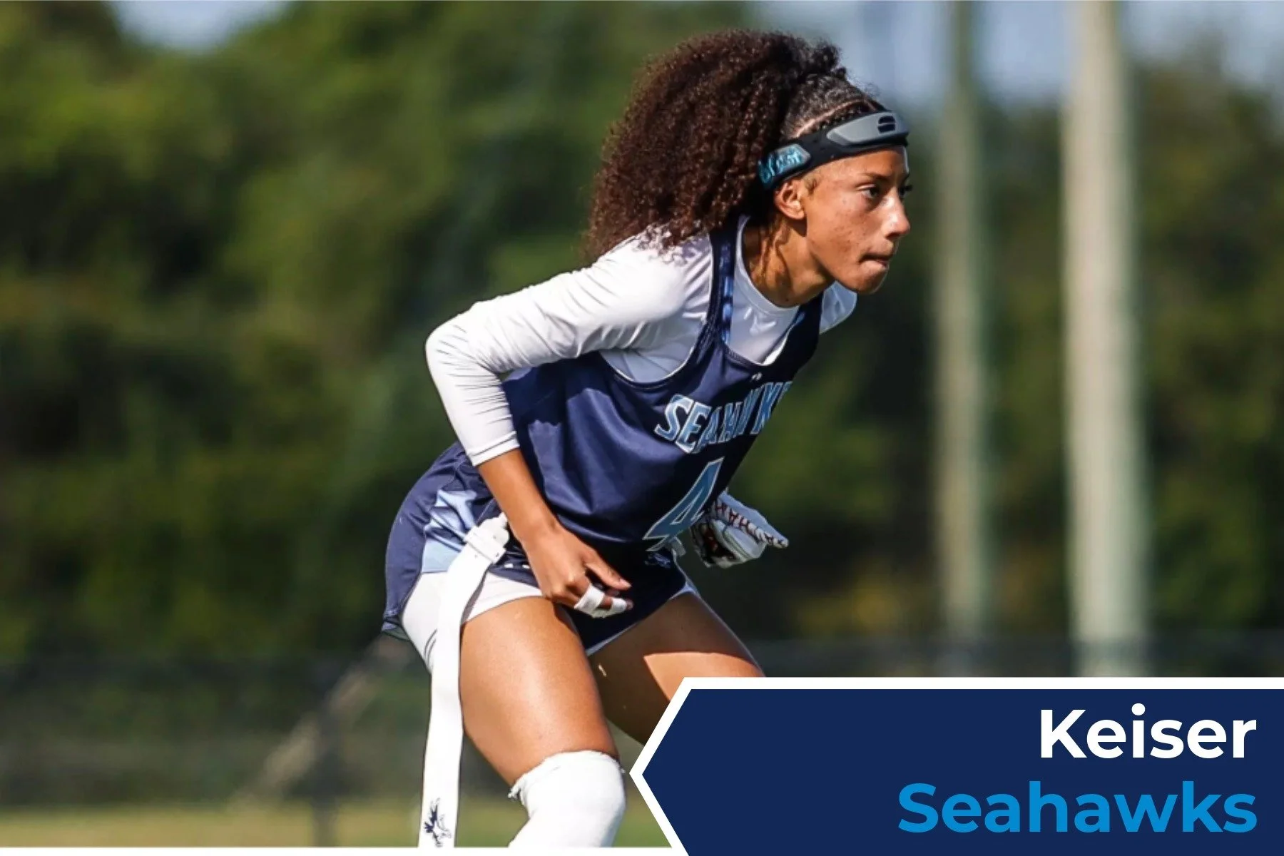 A female football player in a Seattle Seahawks uniform in a ready stance on the field.